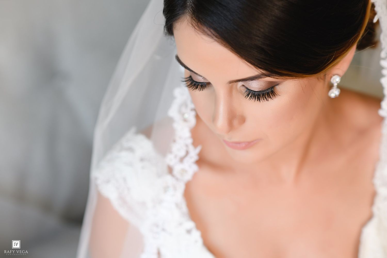 Close-up of bride in lace wedding dress and veil wearing pearl earrings with elegant bridal makeup.