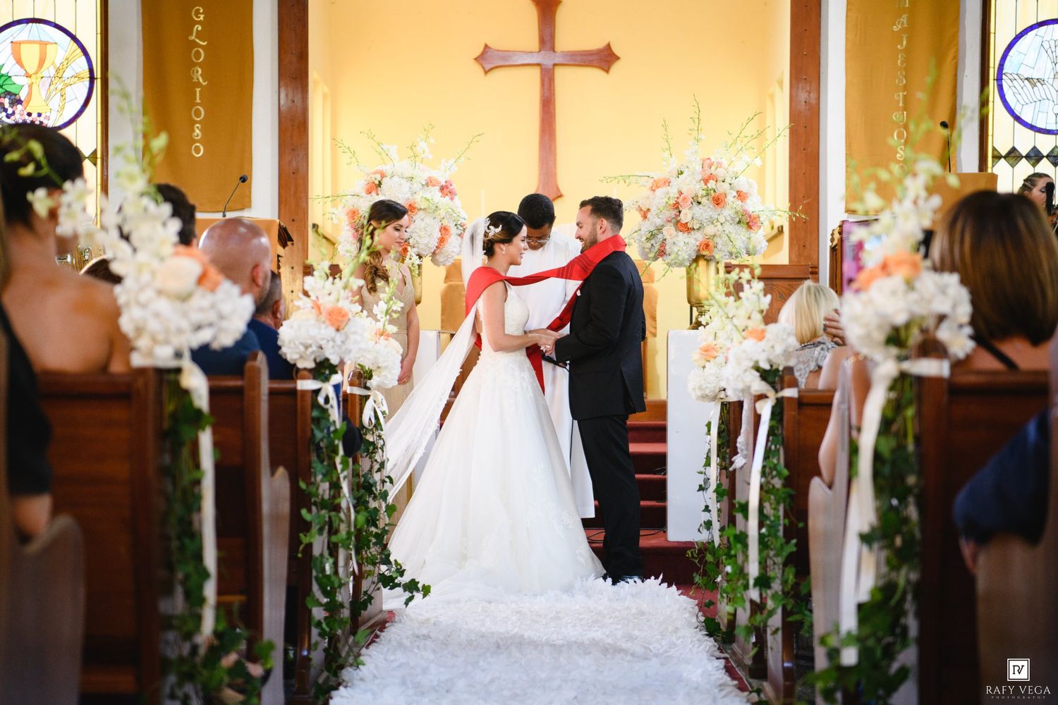 Bride and groom share a romantic moment at the church altar, surrounded by elegant white floral arrangements during their wedding ceremony.