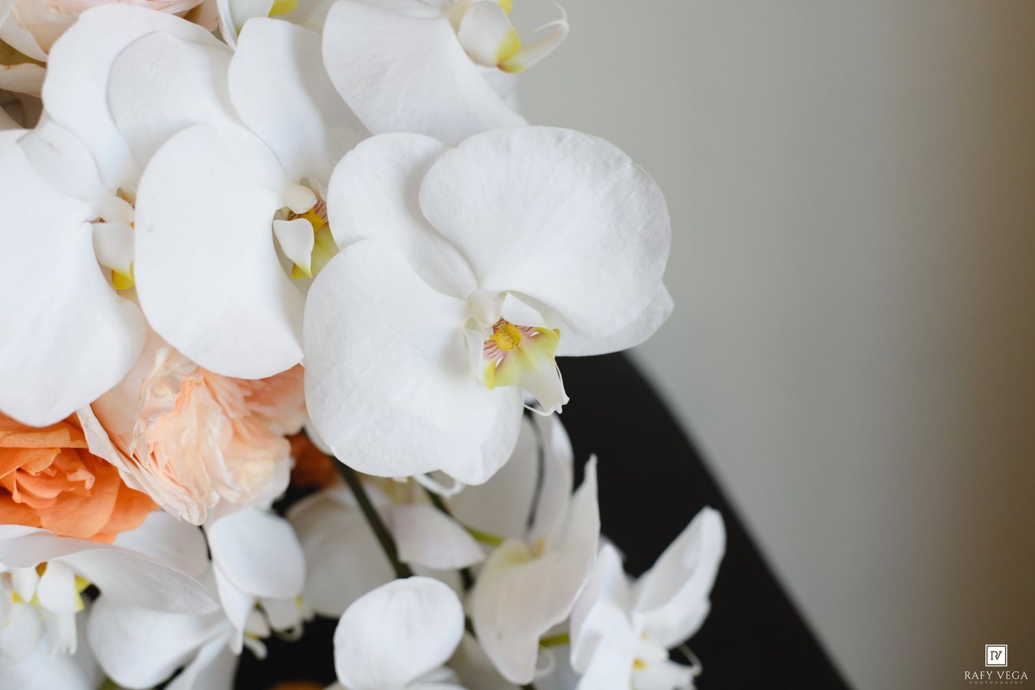 Close-up of elegant white orchids and peach roses arrangement against a soft background.