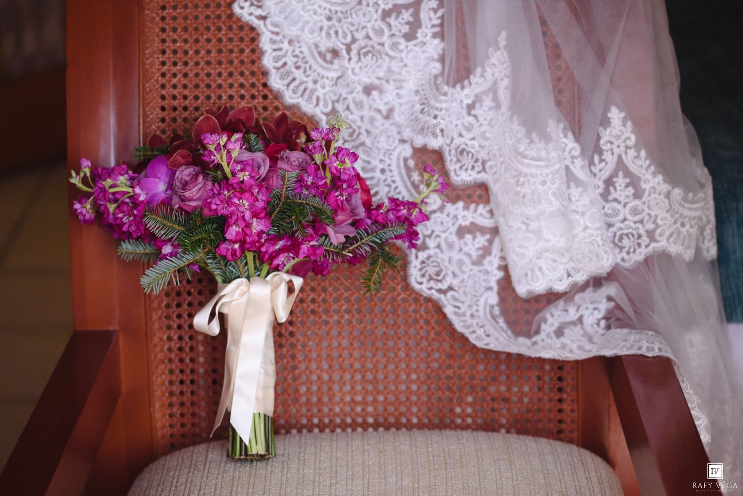 Purple and pink bridal bouquet with lace wedding veil draped over a wooden chair.