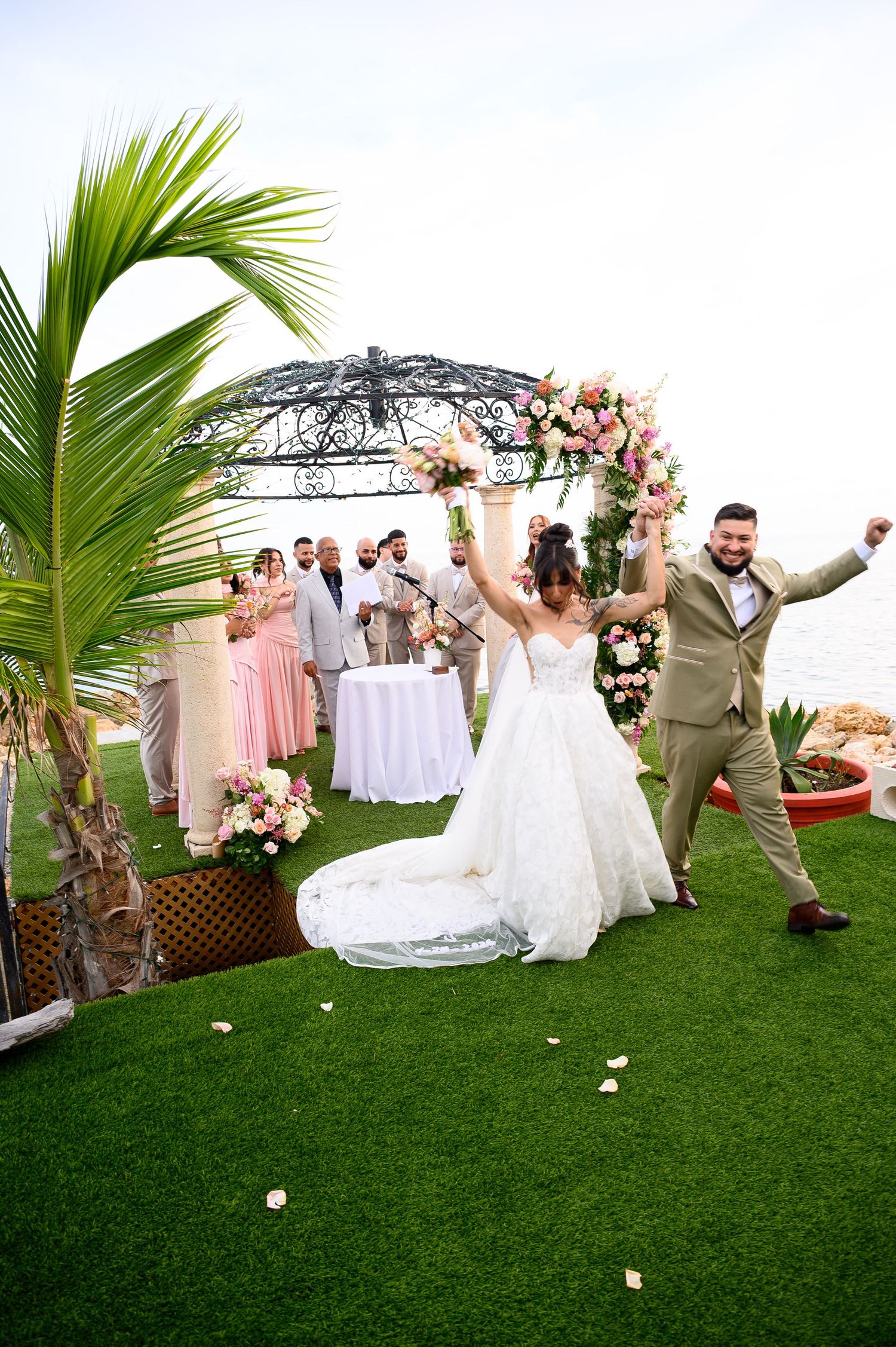 Bride and groom celebrate joyfully at outdoor beach wedding ceremony at Ocean View at Porto Caribe Ponce with floral arch and wedding party.