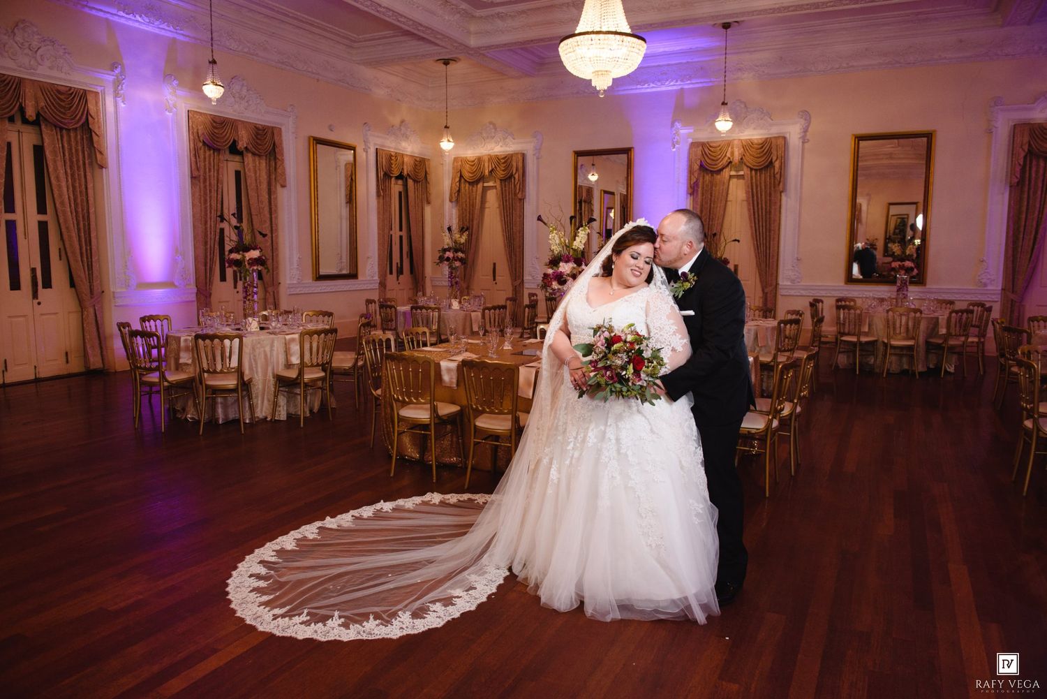 Bride and groom share a romantic pose on the dance floor of an elegant ballroom wedding reception with gold chairs.