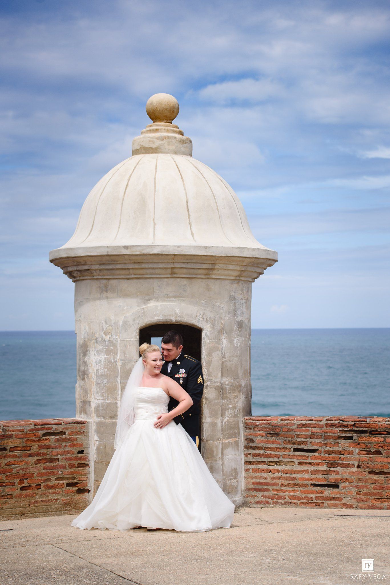 Bride and groom pose romantically by a historic stone sentry tower at El Morro fort with ocean views in Puerto Rico.