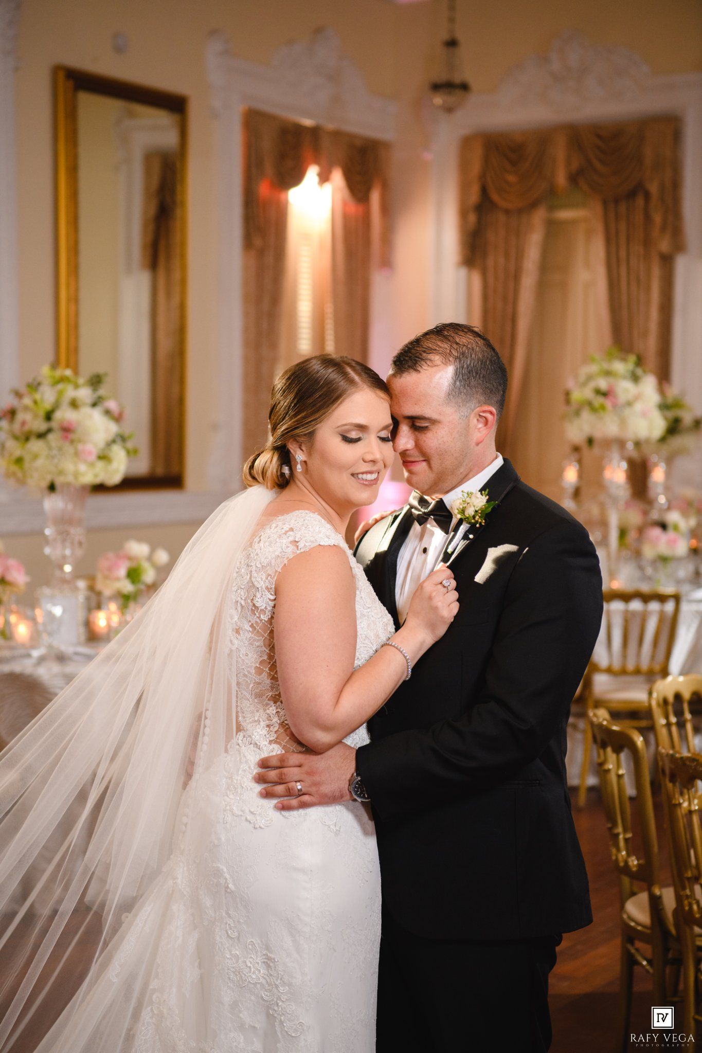 Bride and groom share a romantic moment, embracing tenderly at their elegant wedding reception with floral decor.