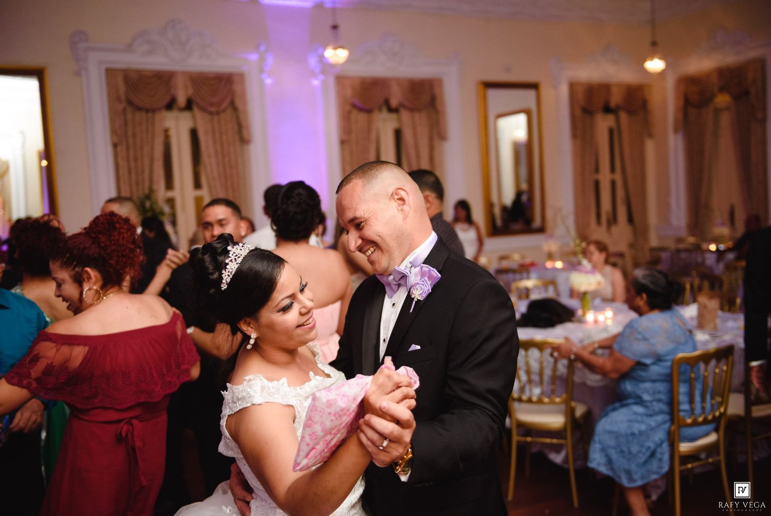 Bride and groom share first dance at wedding reception surrounded by guests in formal attire.