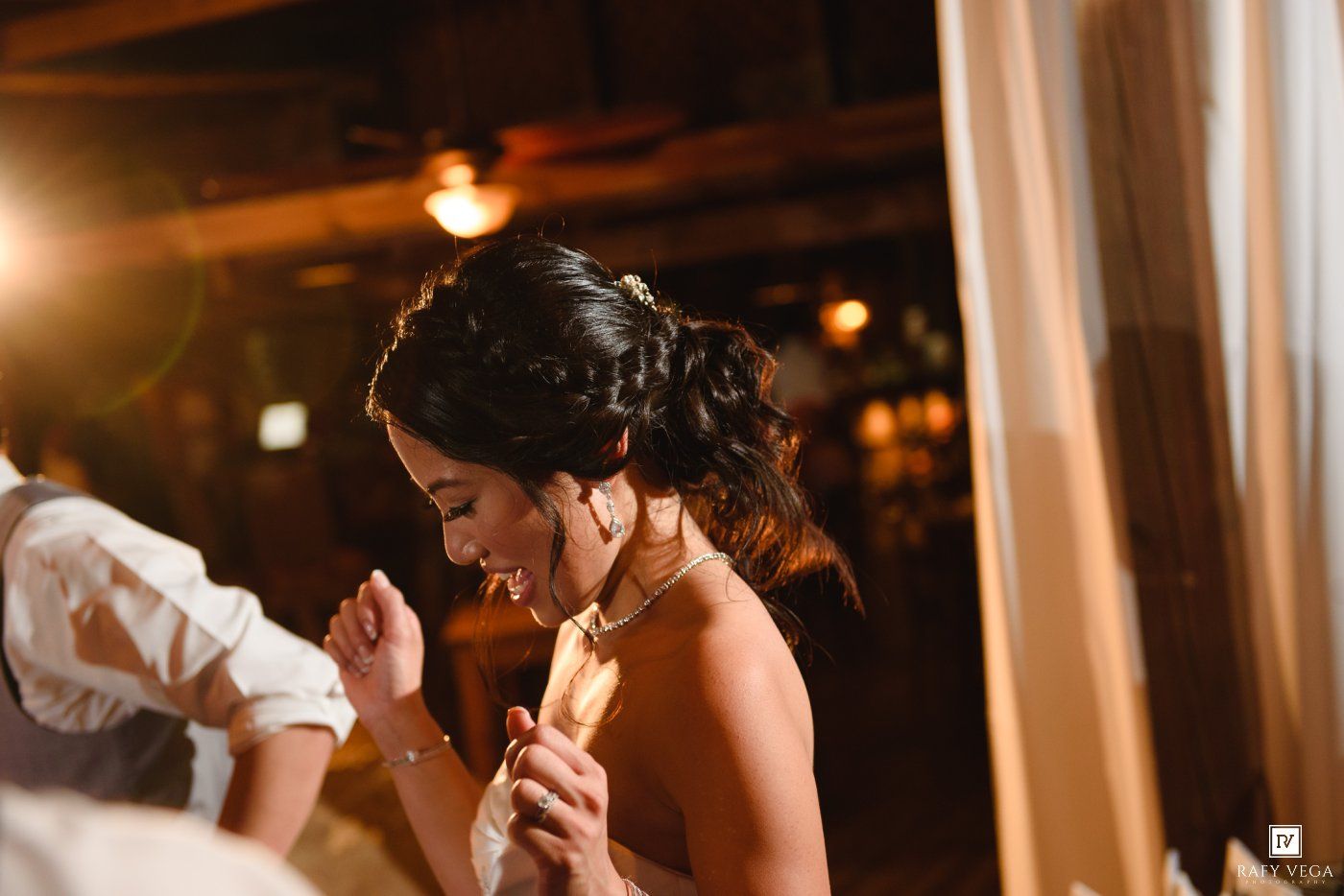 Bride in elegant strapless gown holding a piece of paper at a warmly lit wedding reception.