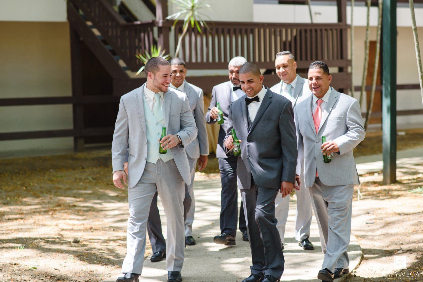 Groomsmen in gray suits walking outdoors at a wedding venue on a sunny day.
