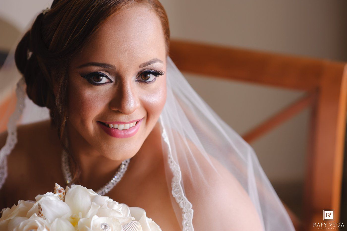Smiling bride in white veil holding a bouquet of white flowers on her wedding day.