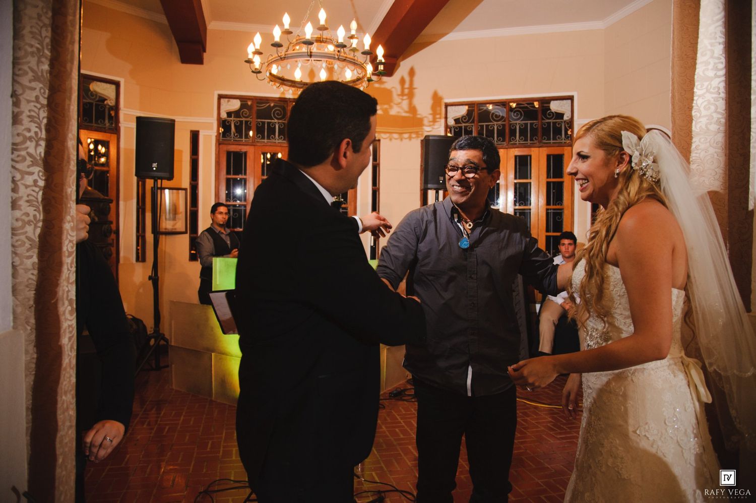 Wedding couple greeting a guest inside a elegant chandelier-lit venue during their reception.