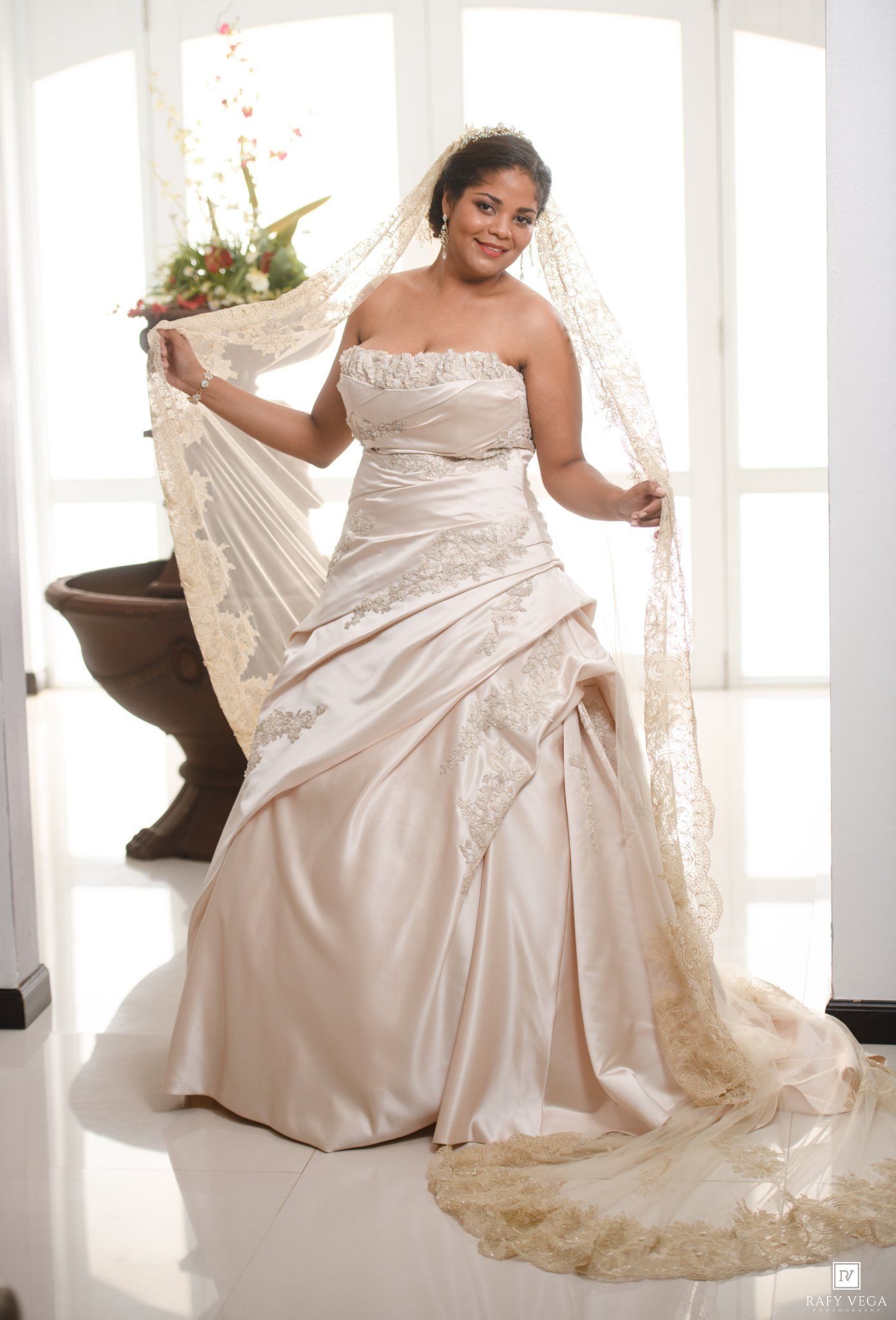 Plus size bride in champagne satin strapless wedding gown with gold lace veil and embroidered train.