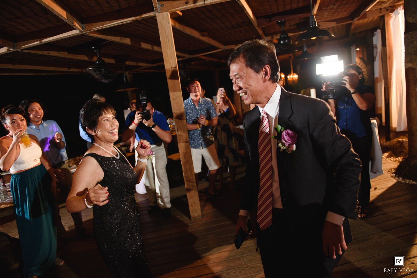 Older couple smiles and dances together joyfully at a warm indoor wedding reception.