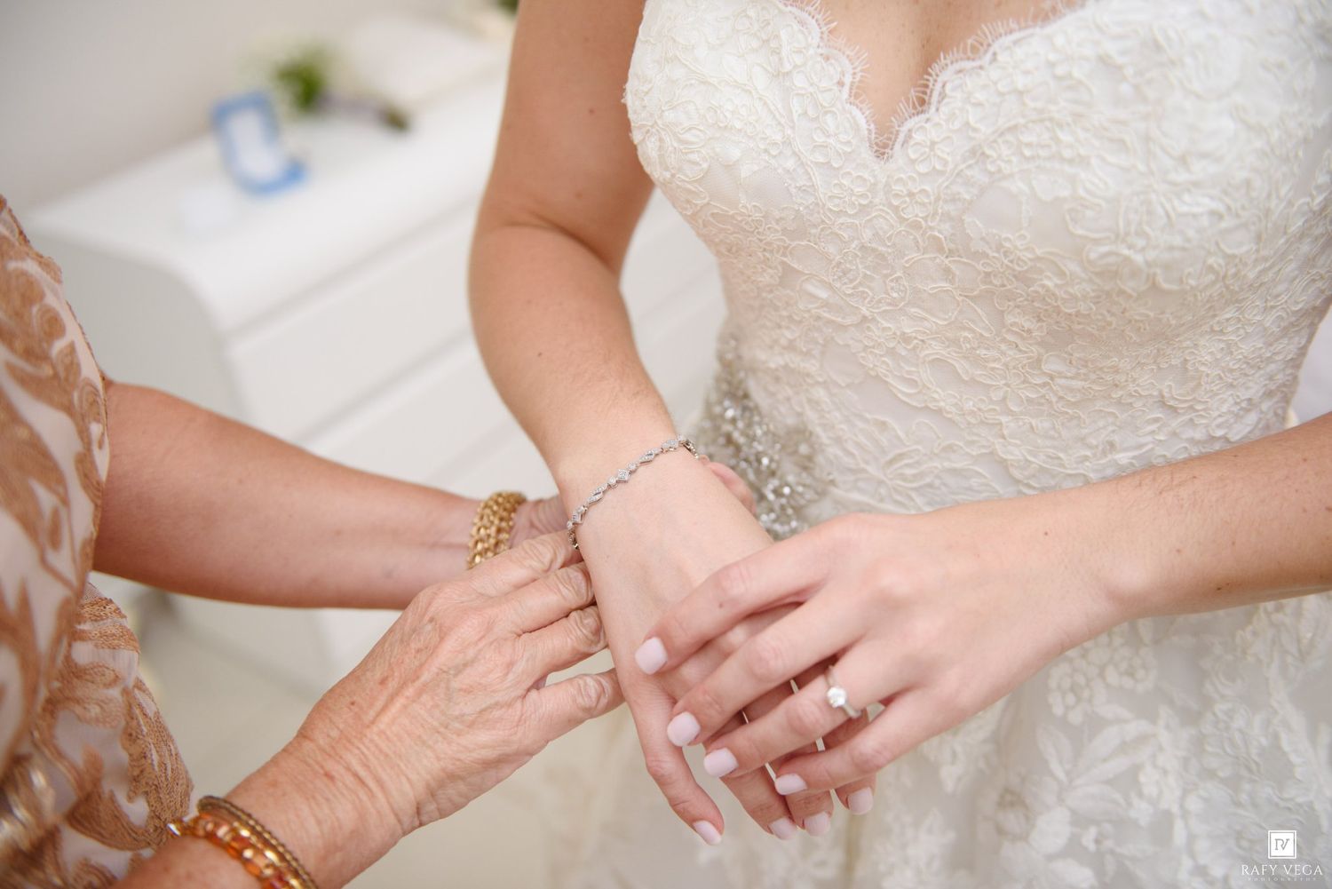 Elderly woman fastening a crystal bracelet on a bride wearing a white lace wedding gown.