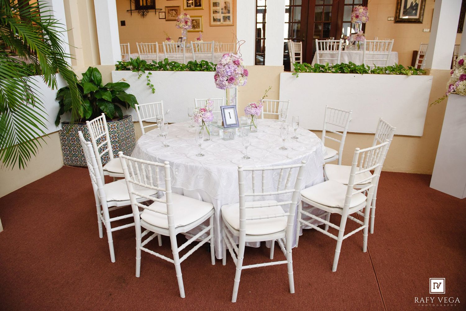 Elegant white round banquet table with Chiavari chairs and floral centerpiece set for a wedding reception indoors.