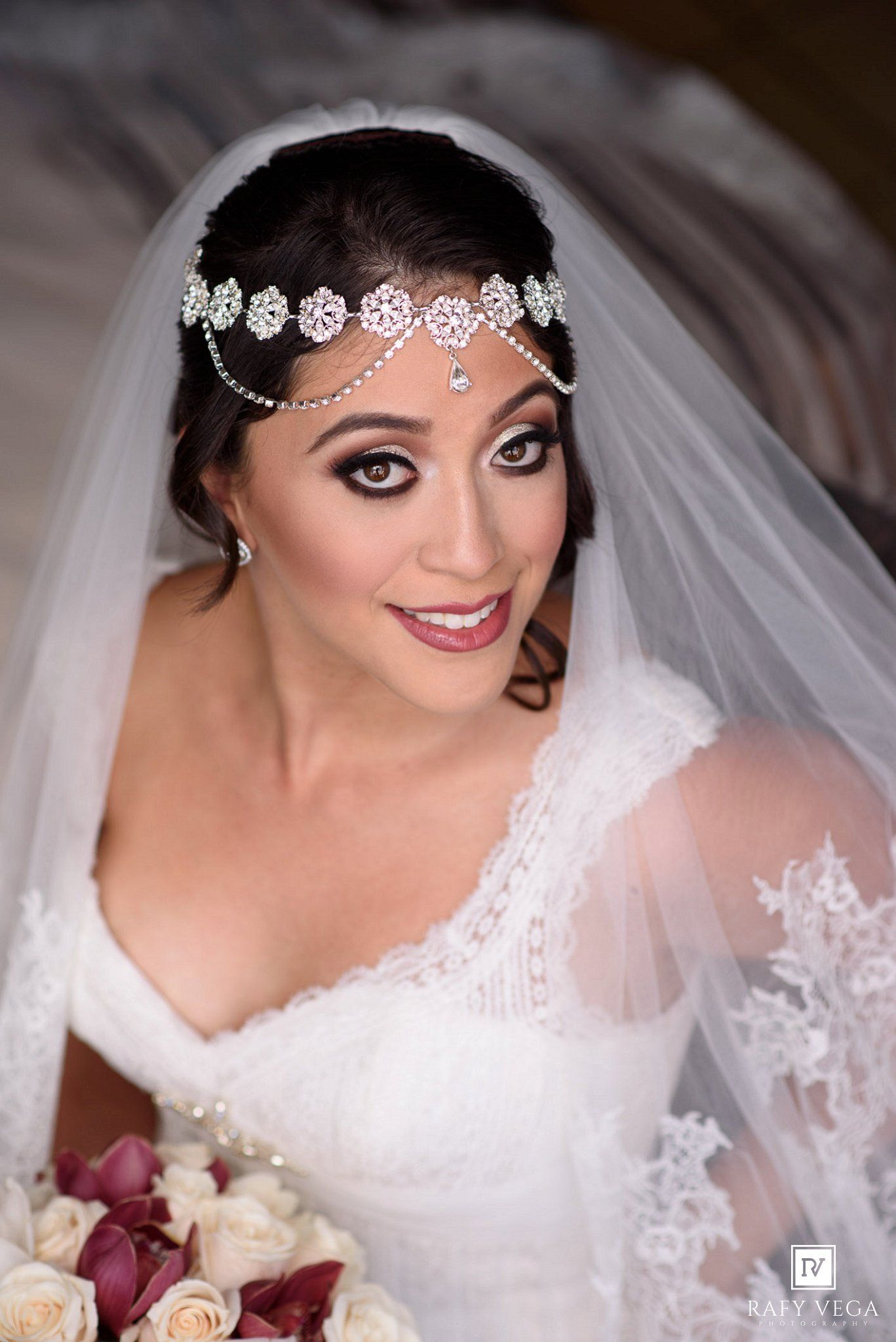 Bride wearing lace wedding dress, jeweled headpiece, and veil, holding white roses bouquet.