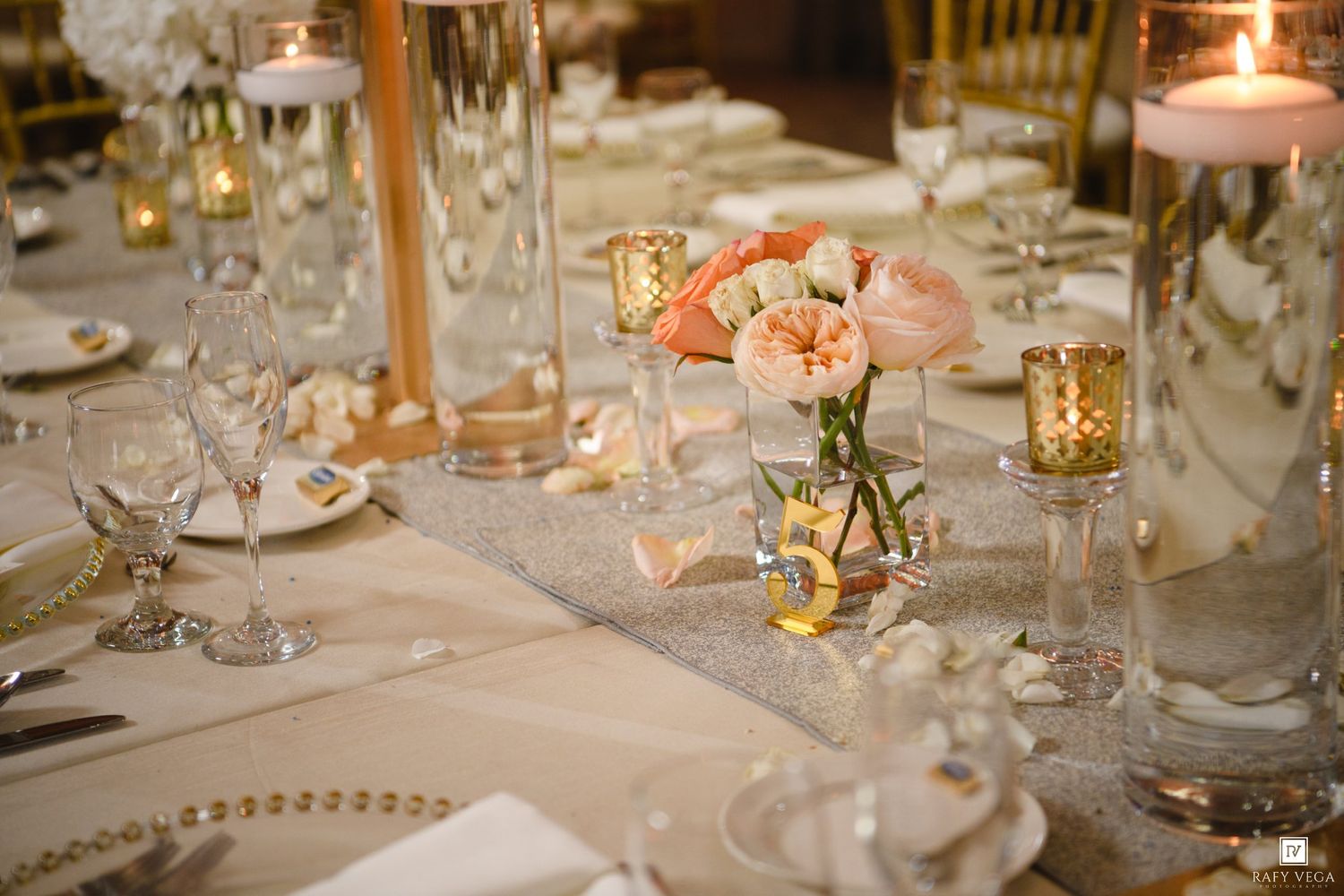 Elegant wedding reception table with pink floral centerpiece, gold candles, crystal glasses, and shimmering table runner.