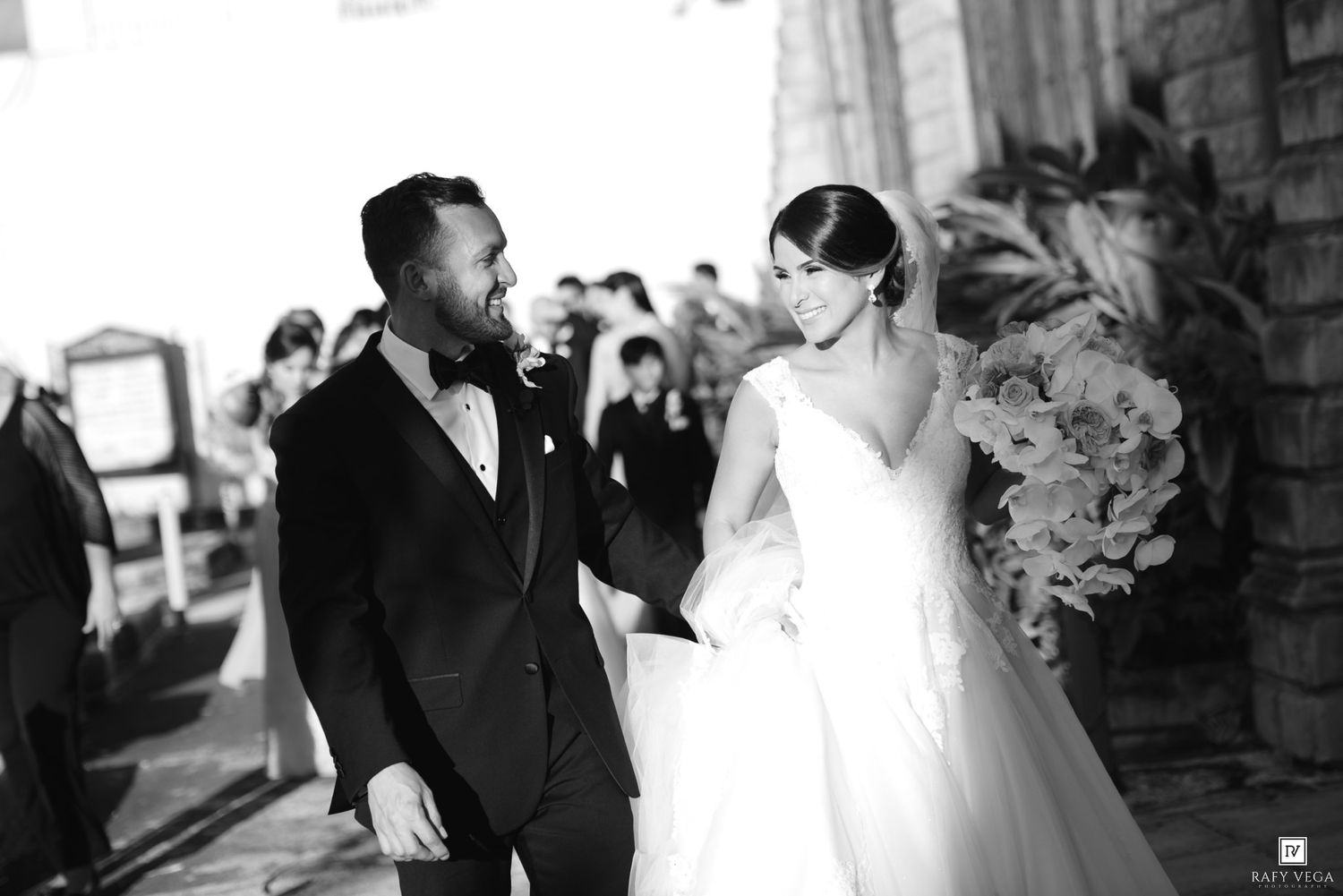 Black and white photo of a smiling bride and groom holding hands outside their wedding ceremony venue.