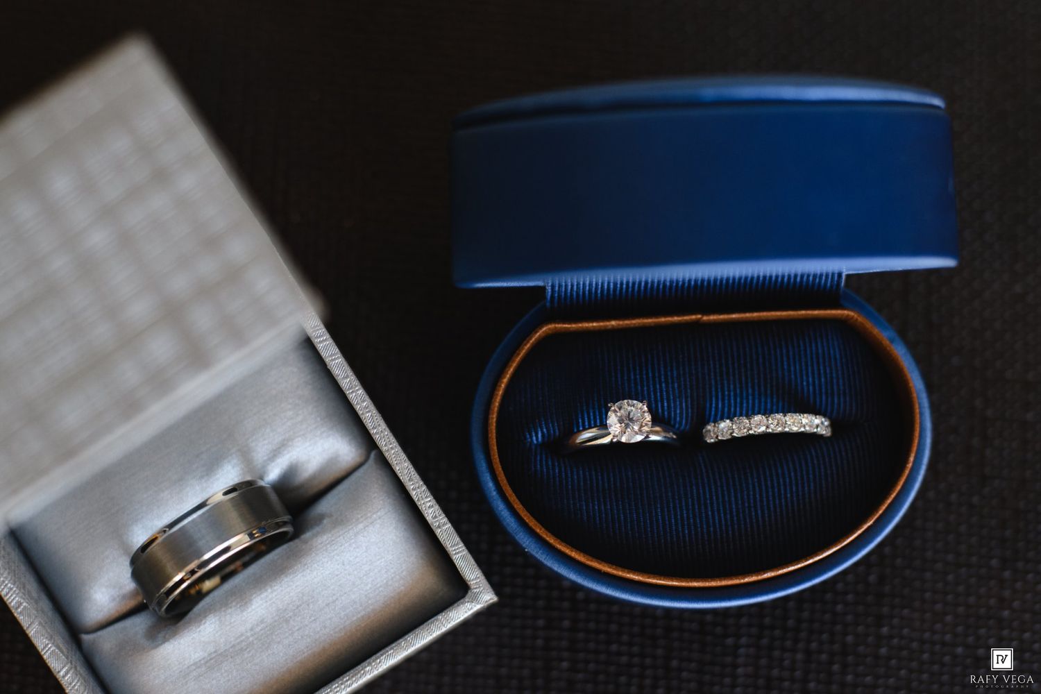 Wedding rings displayed in elegant boxes, featuring a diamond engagement ring and band in a blue velvet ring box.