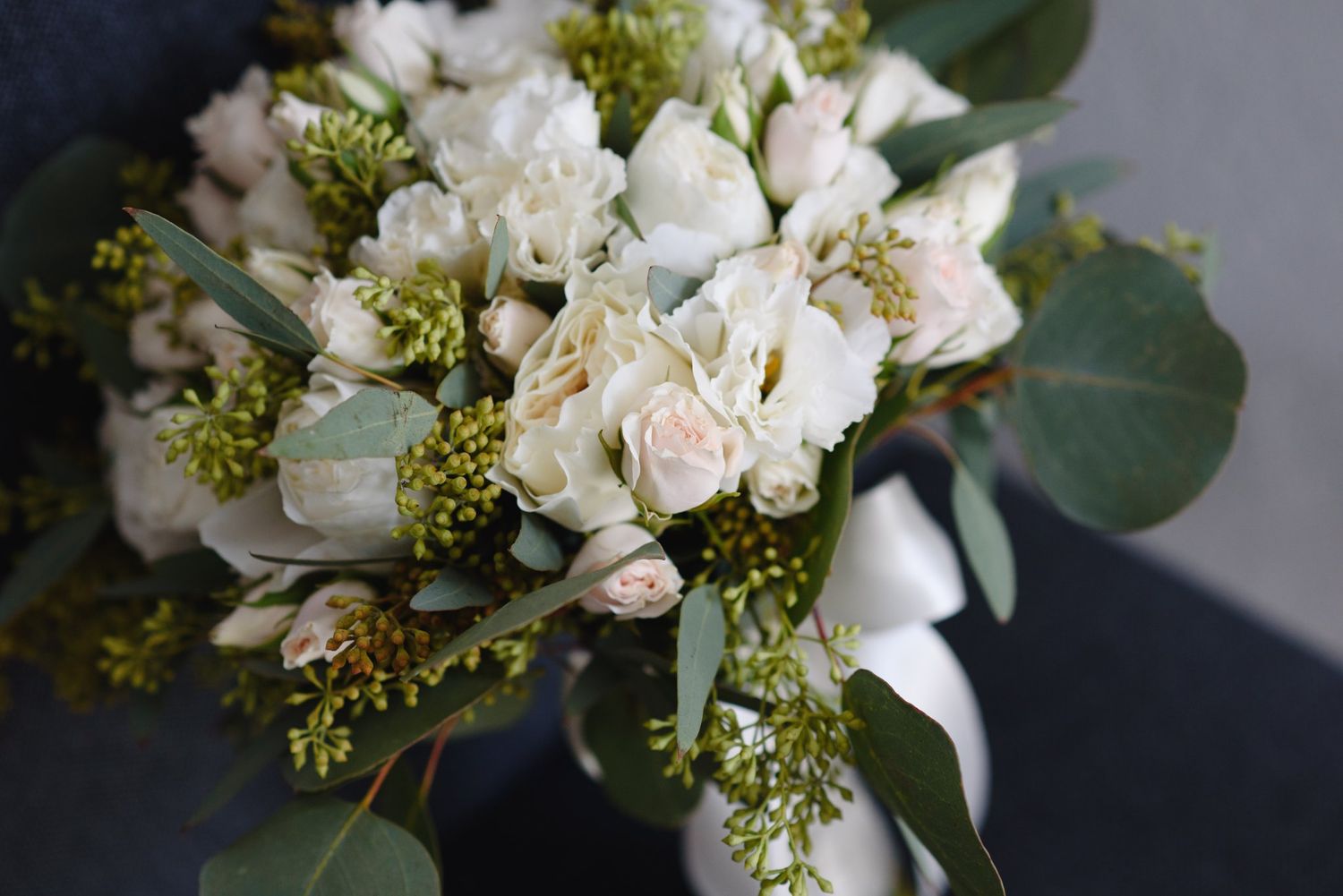 Elegant bridal bouquet featuring white roses, eucalyptus, and green berries tied with white ribbon.