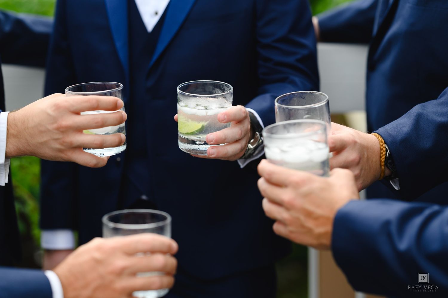 Men in suits toasting with cocktail glasses at a formal wedding celebration event.