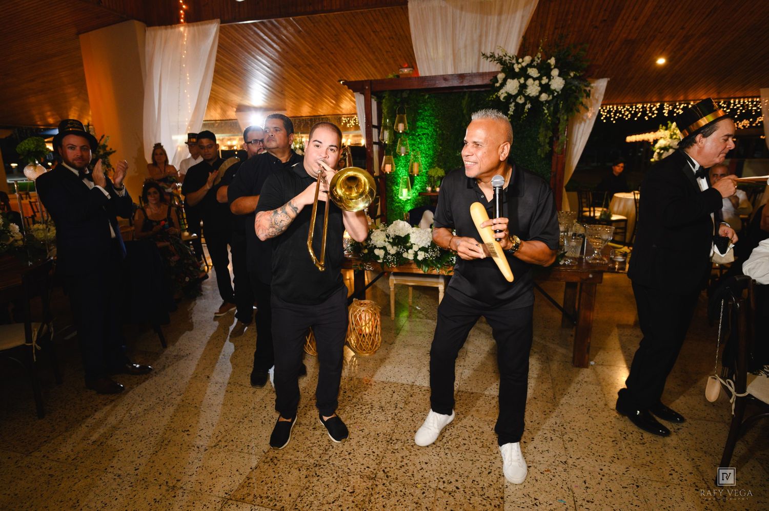 Live band performing at wedding reception, musicians in black outfits playing trumpet and maracas on dance floor.