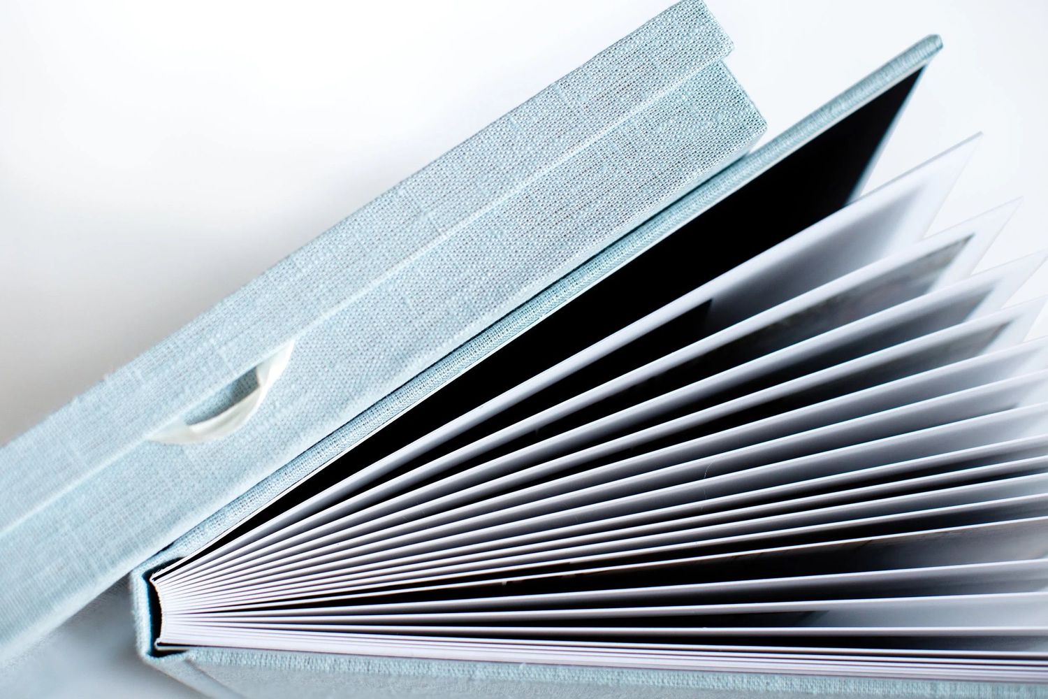 Light blue hardcover book open and fanned out, showing white pages from a side angle on white background.