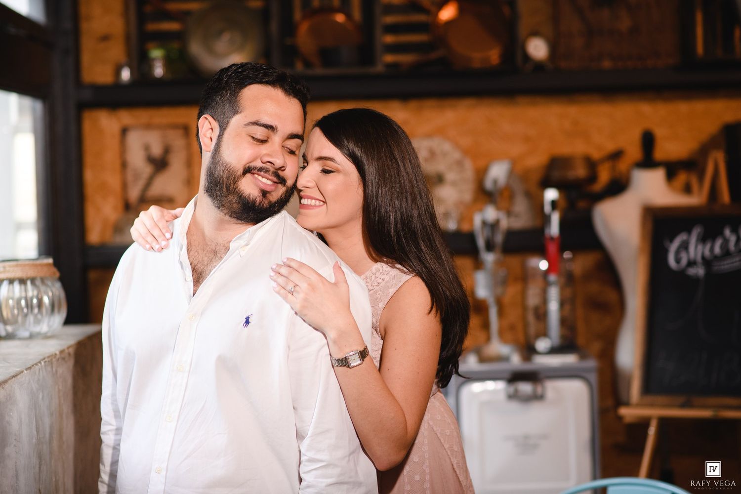 Couple embracing romantically in a rustic cafe setting, man in white shirt with woman smiling joyfully.