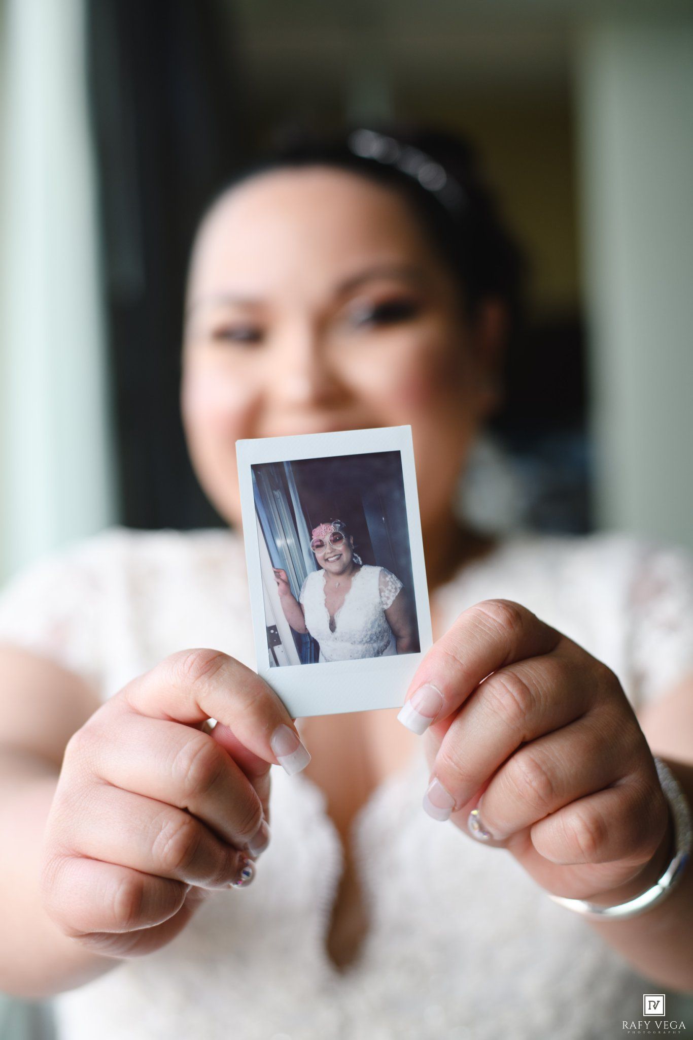 Bride in white dress holds a Polaroid photo on her wedding day, showcasing a candid portrait moment.