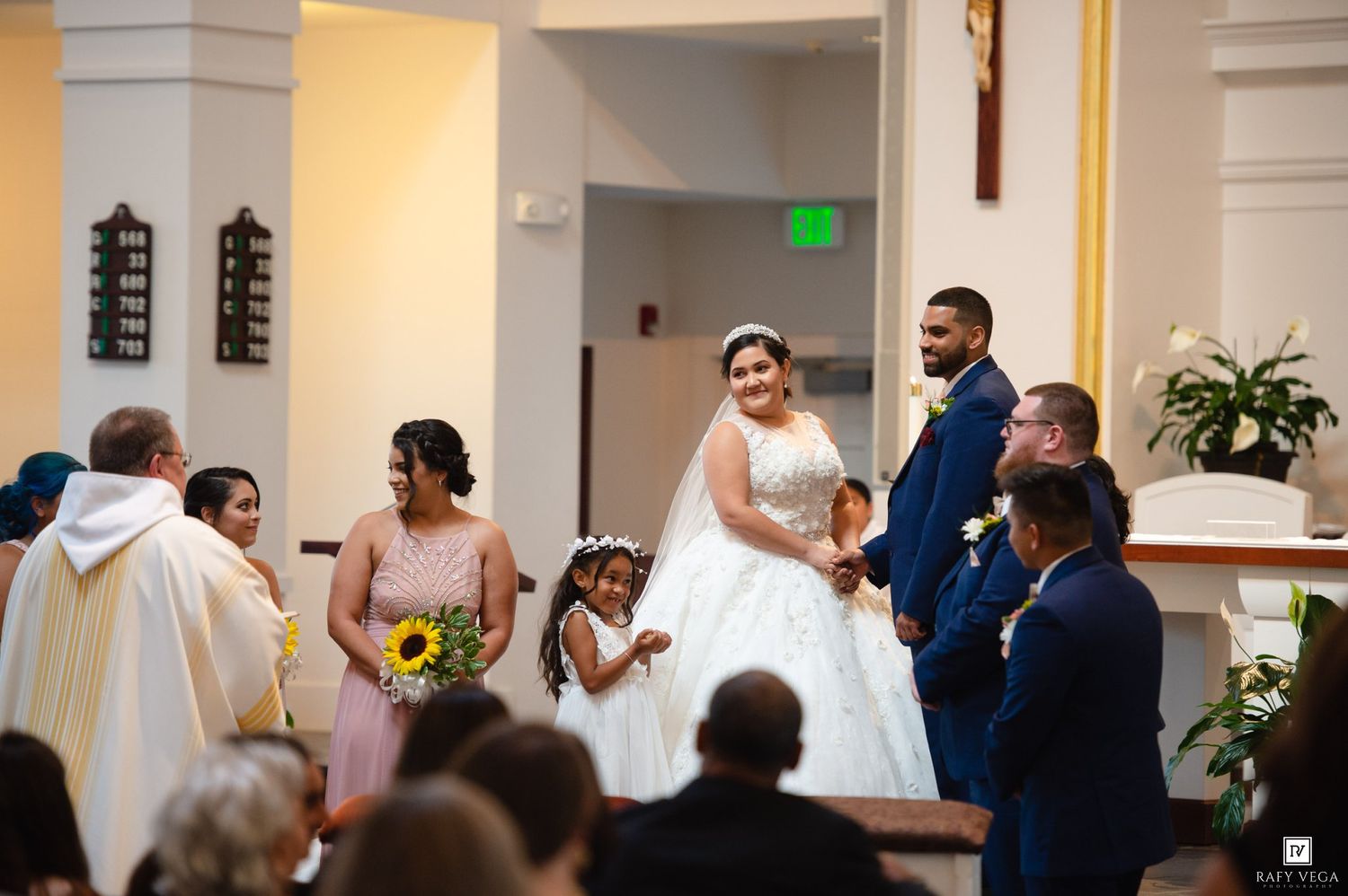 Bride and groom share a joyful moment at the altar during a church wedding ceremony with bridesmaids and flower girl.