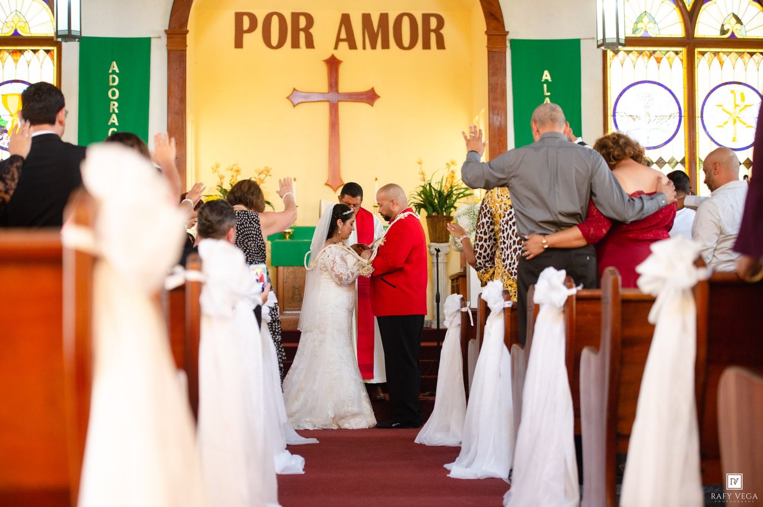 Wedding ceremony in church with officiant and couple at altar under Por Amor banner.