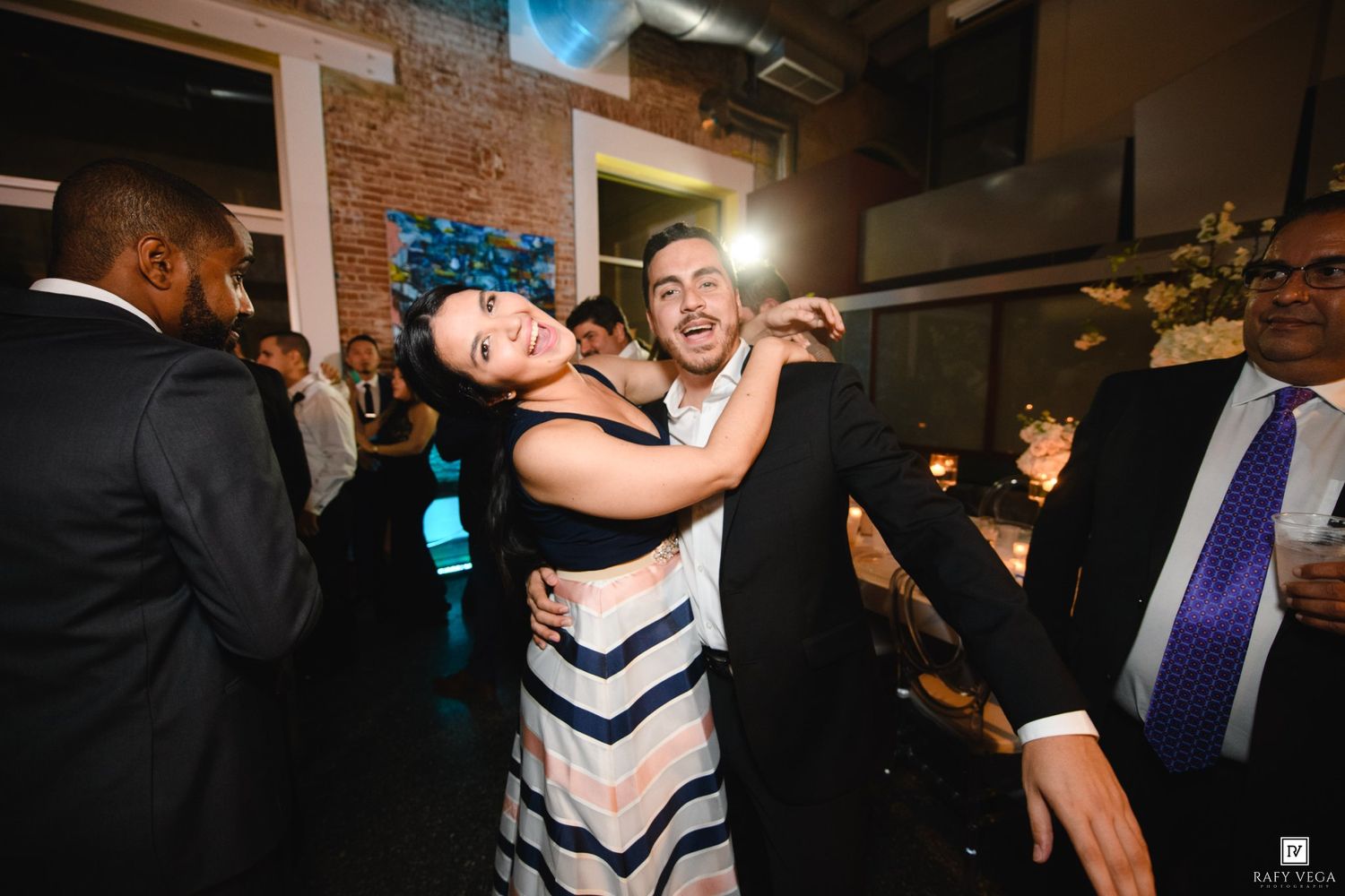 Couple dancing and embracing joyfully at an elegant indoor wedding reception with guests in formal attire.