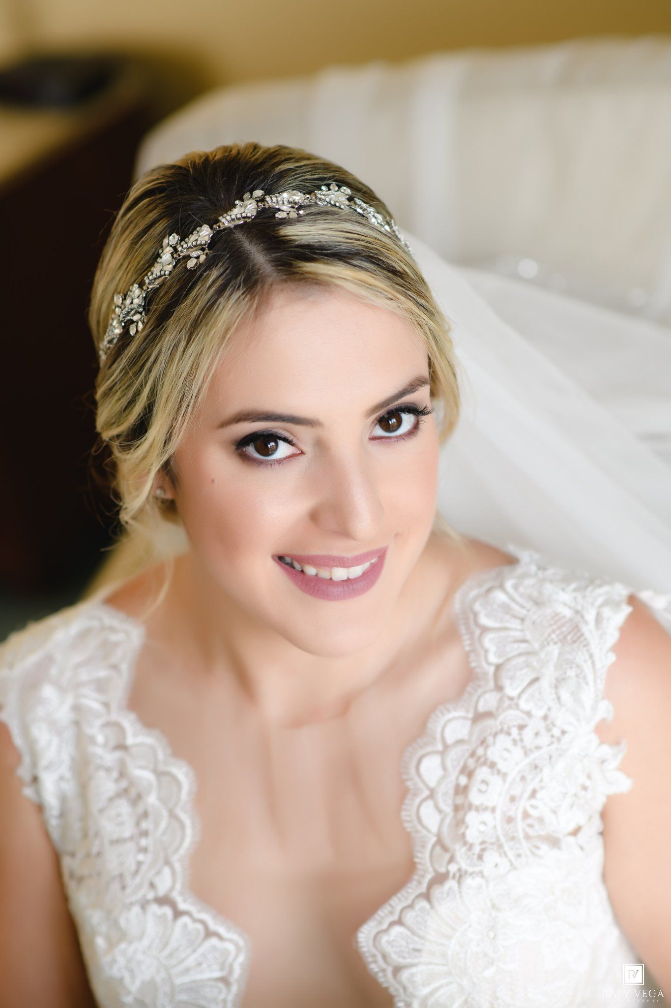 Bride wearing lace gown and crystal tiara headpiece with veil, smiling elegantly on her wedding day.