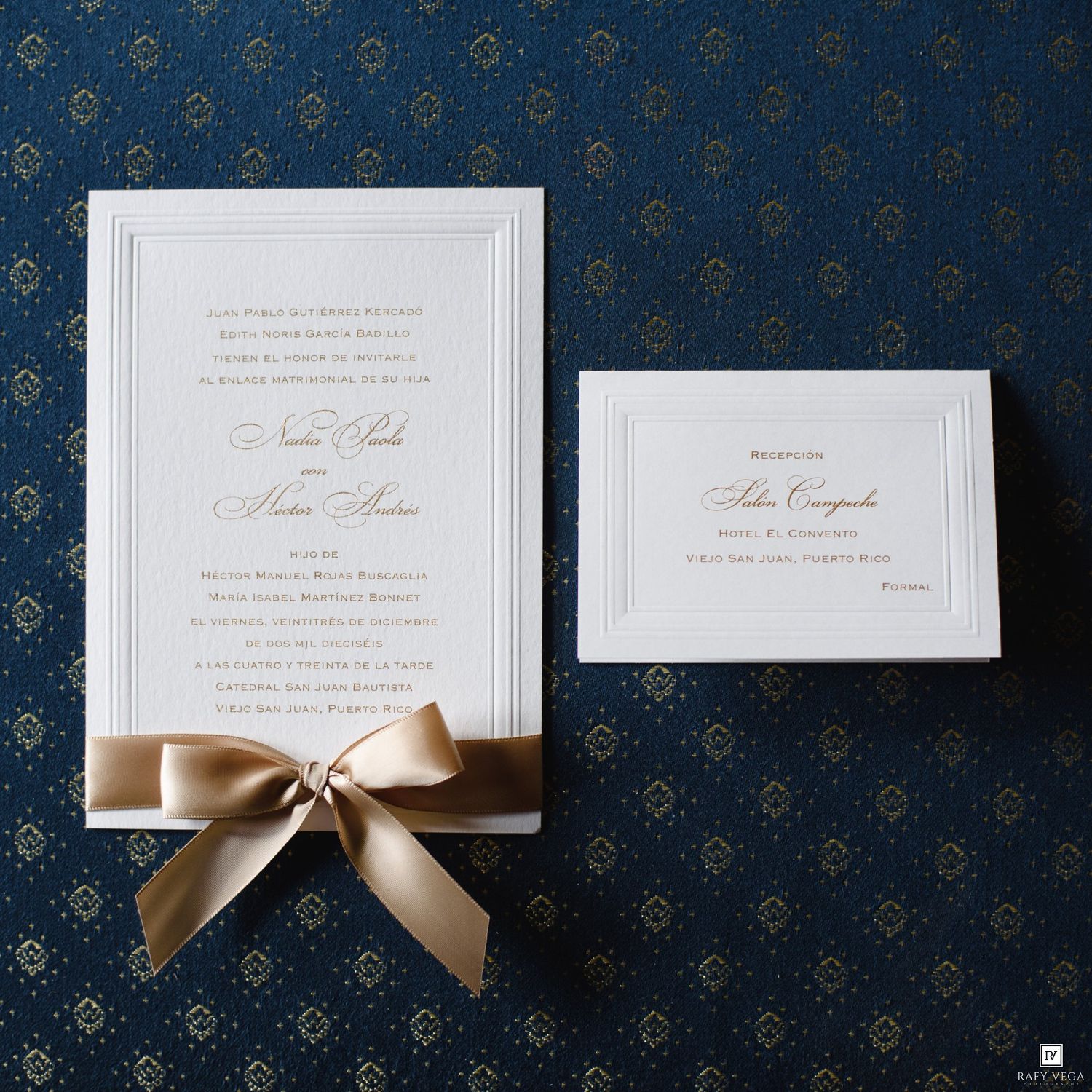 Elegant wedding invitation suite with gold ribbon bow and matching enclosure card on navy blue background.