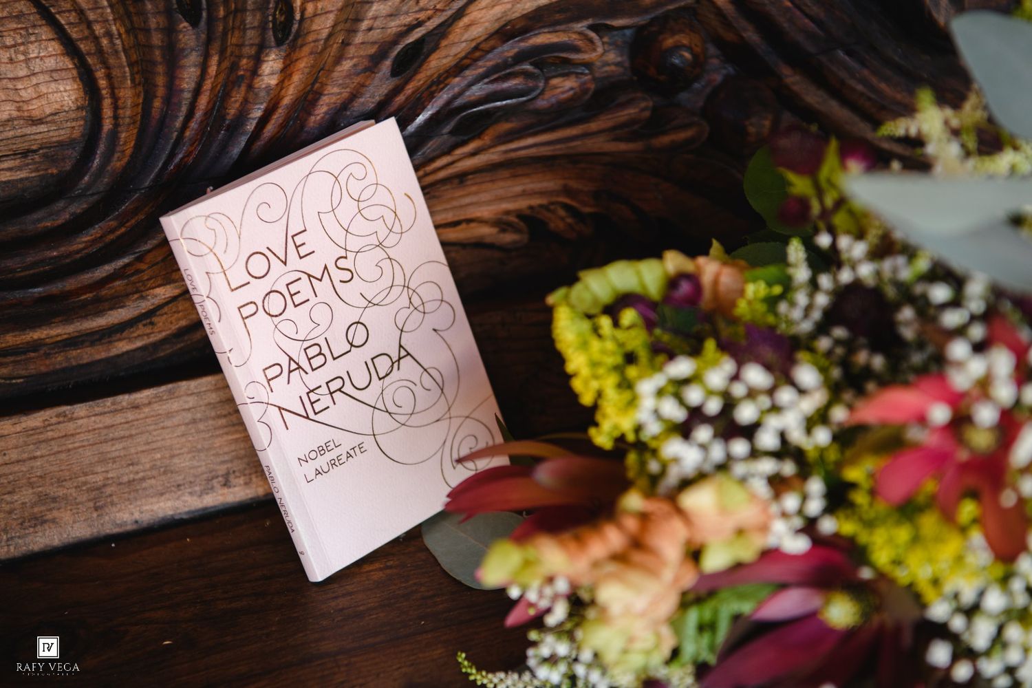 Love Poems by Pablo Neruda book beside a colorful floral bouquet on a rustic wooden bench.