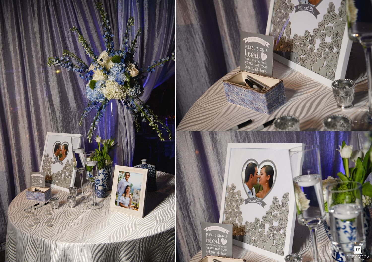 Elegant wedding reception table with floral arrangement, framed photos, and decorative guest book display in blue and silver.