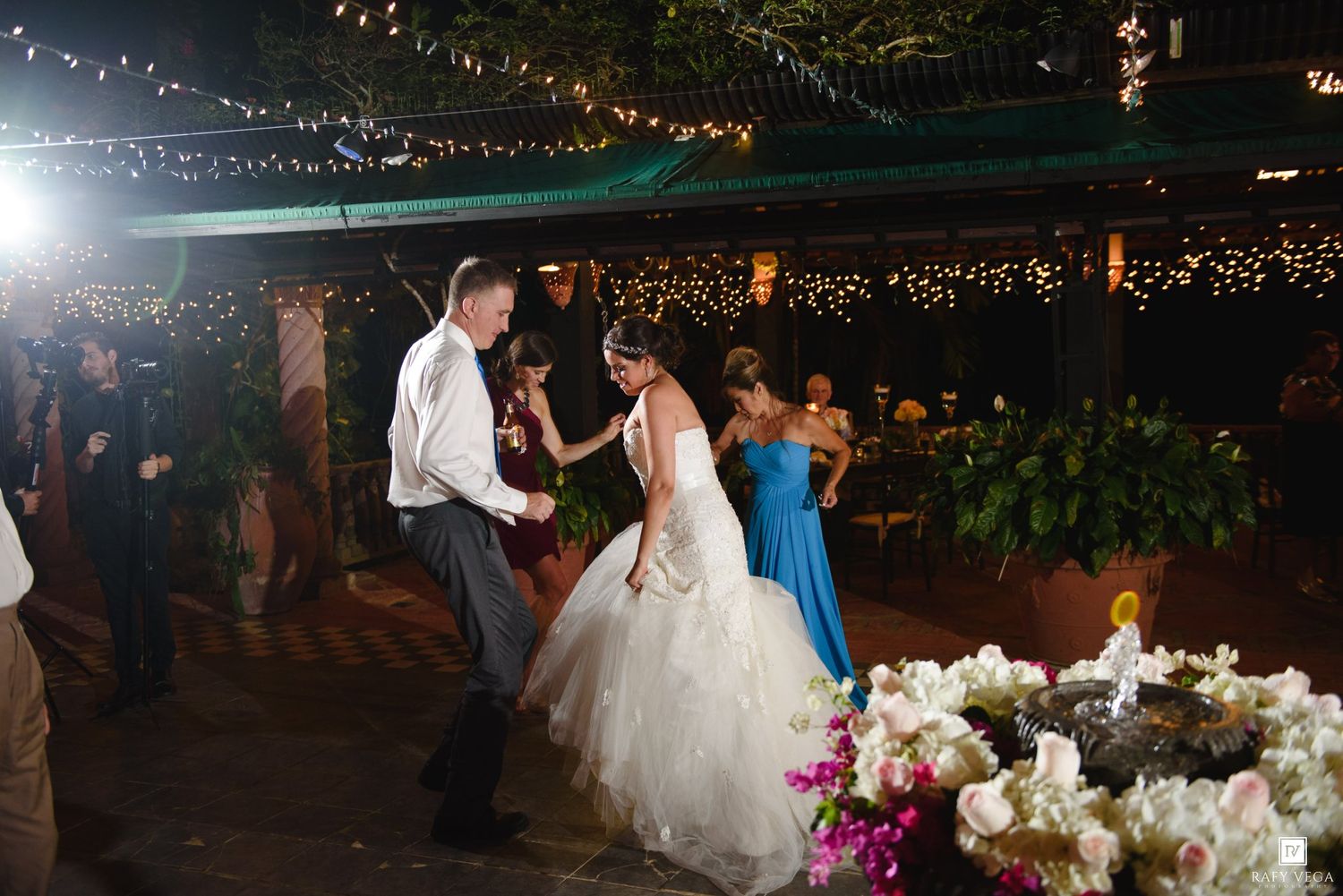 Bride and groom share a dance at an outdoor wedding reception with string lights and floral arrangements.