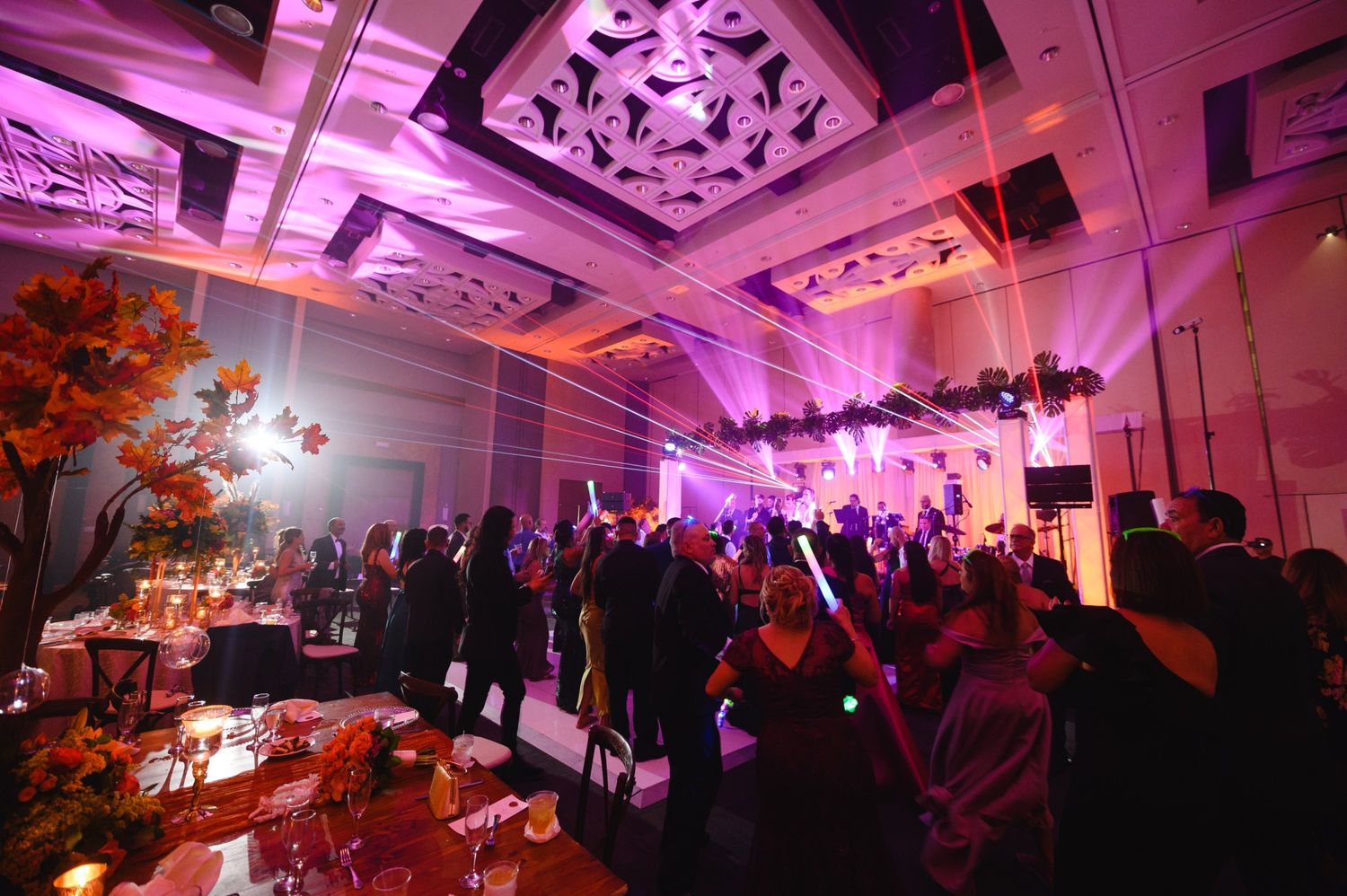 Elegant gala event with purple lighting, autumn floral arrangements, and guests mingling in a grand ballroom.