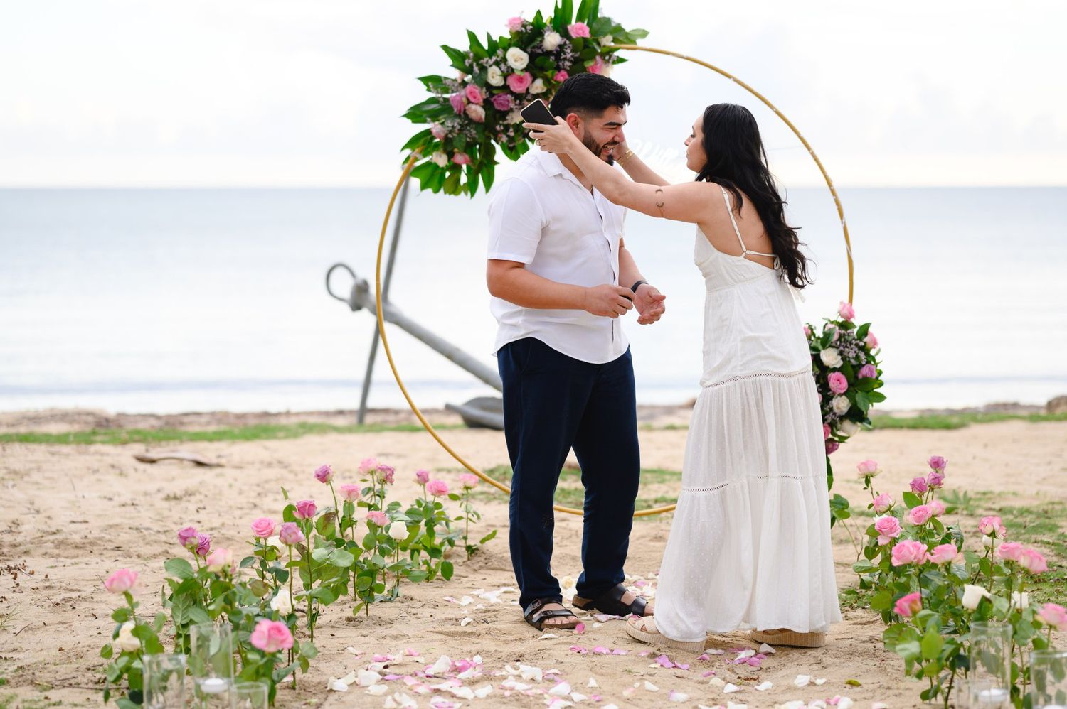Couple exchanging vows on a beach wedding ceremony with floral hoop arch and pink roses.