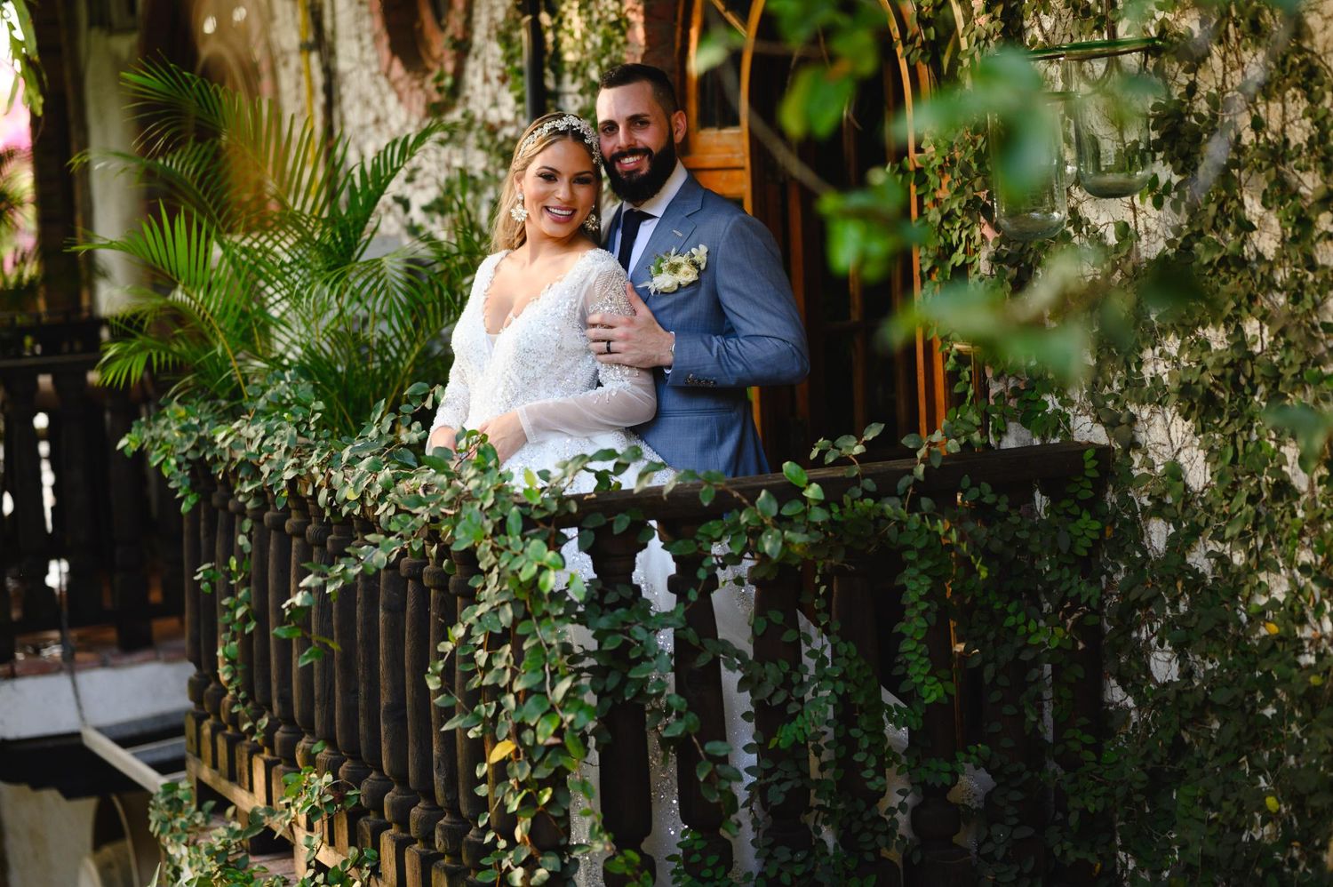 Bride and groom posing on an ivy-covered balcony surrounded by lush greenery on their wedding day.