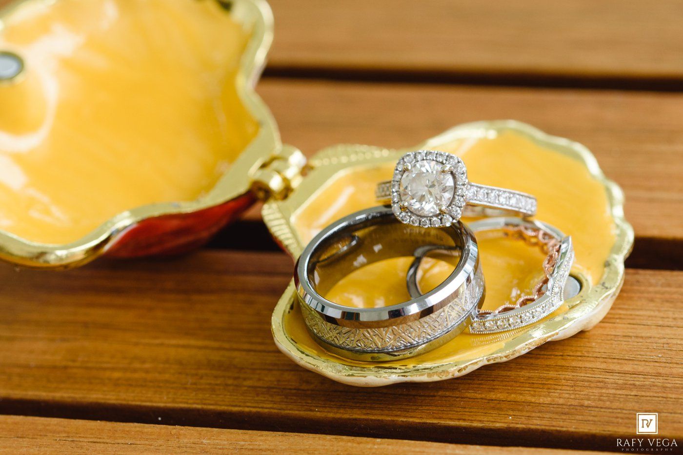 Three elegant wedding rings displayed in a yellow decorative shell-shaped jewelry box on a wooden surface.