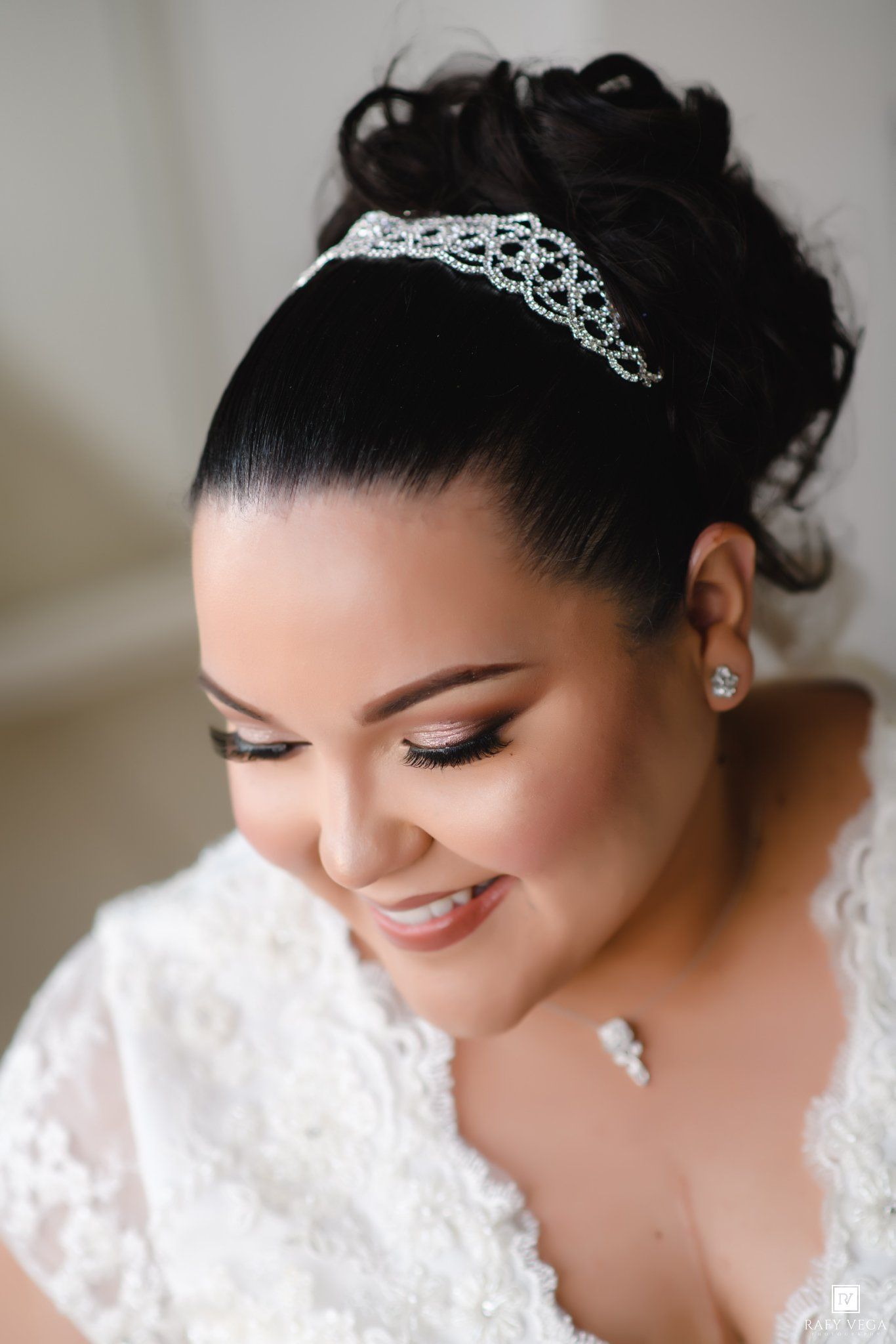 Bride wearing a sparkling tiara and lace wedding dress, with elegant updo hairstyle and glam makeup, smiling softly.