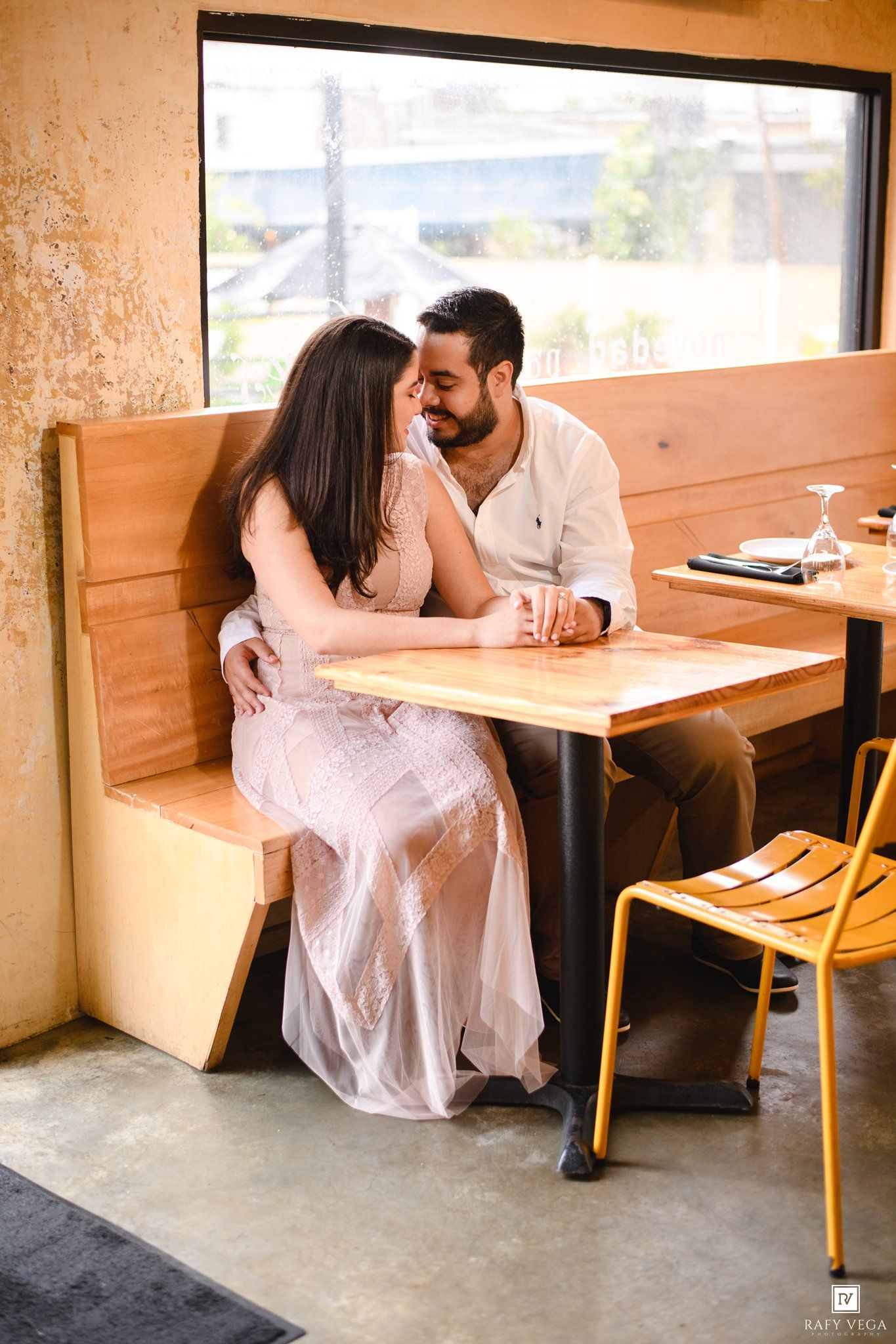 Couple sharing a romantic moment at a wooden booth table in a cozy restaurant, smiling at each other.