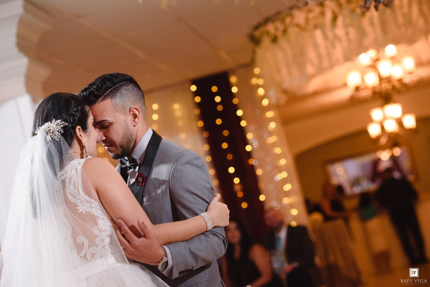 Bride and groom share first dance at romantic wedding reception with warm bokeh lights.