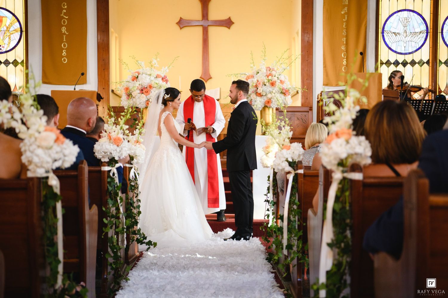 Bride and groom exchange vows at a church altar adorned with white and pink floral arrangements during a wedding ceremony.
