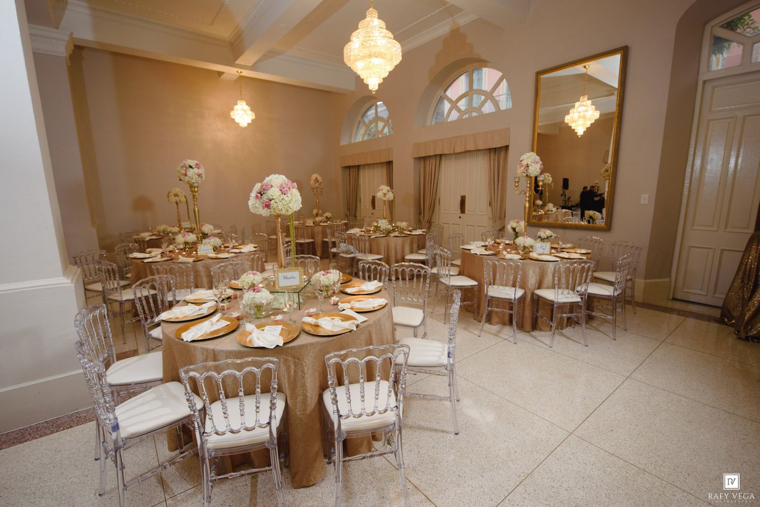 Elegant wedding reception hall with gold round tables, chiavari chairs, and floral centerpieces.