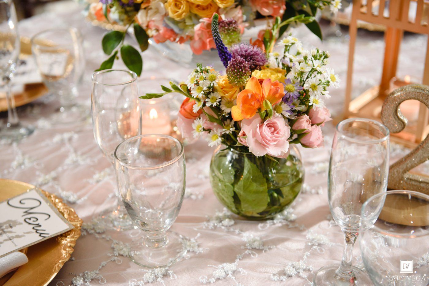 Elegant wedding table centerpiece with colorful pink, orange, and purple flowers in a green vase with candles.