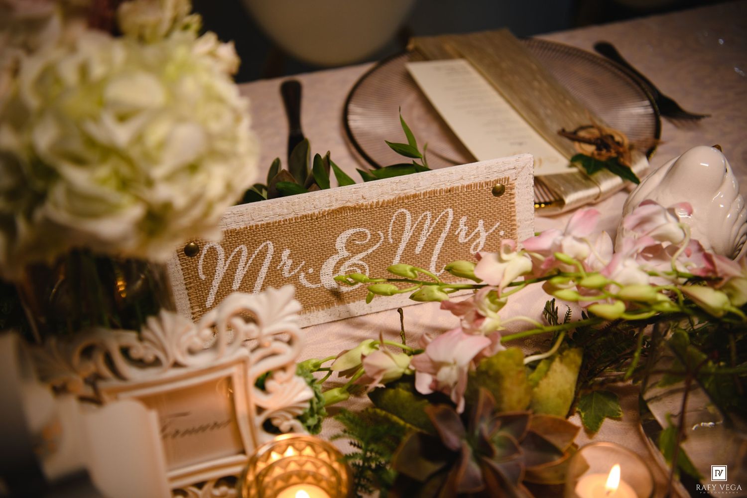 Elegant wedding sweetheart table decorated with Mr. & Mrs. sign, white flowers, and greenery arrangements.