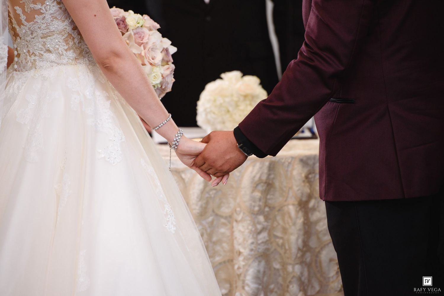 Bride and groom holding hands during wedding ceremony, bride holding white floral bouquet in elegant ballgown.