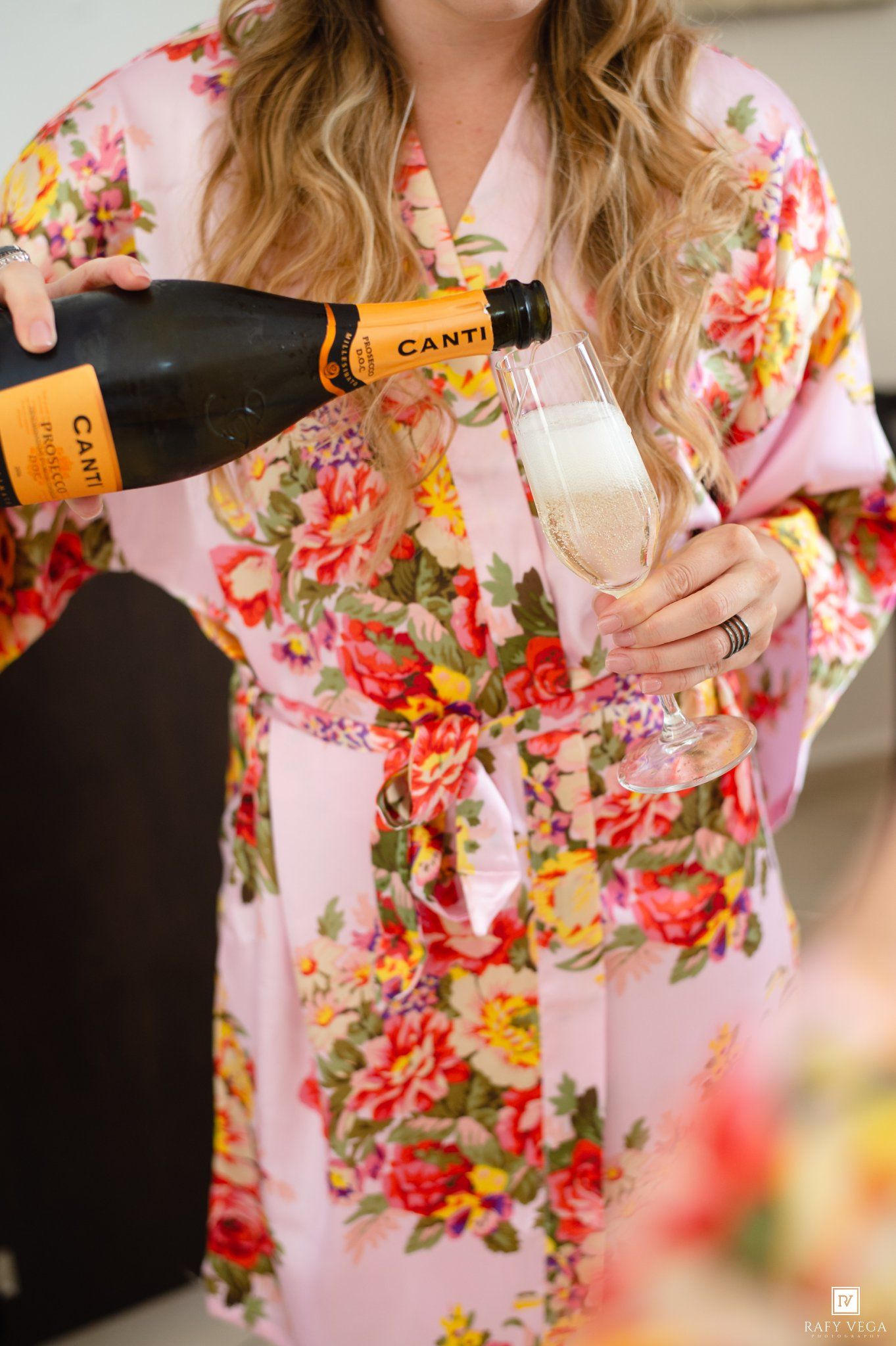 Woman in pink floral robe pouring Canti sparkling wine into a champagne flute.