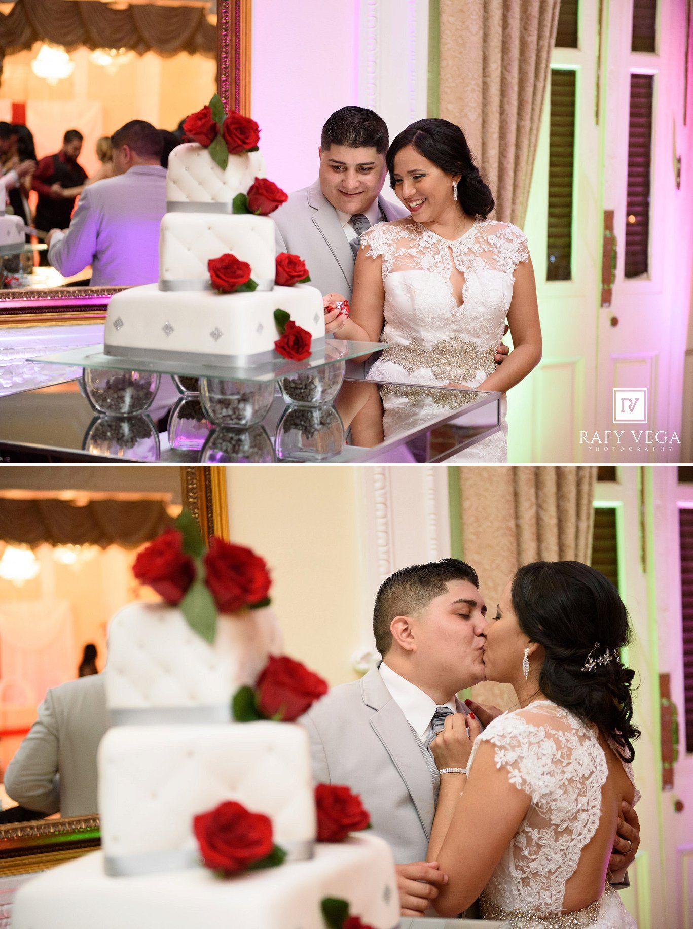 Newlyweds cut and kiss beside a white wedding cake adorned with red roses at their elegant reception.