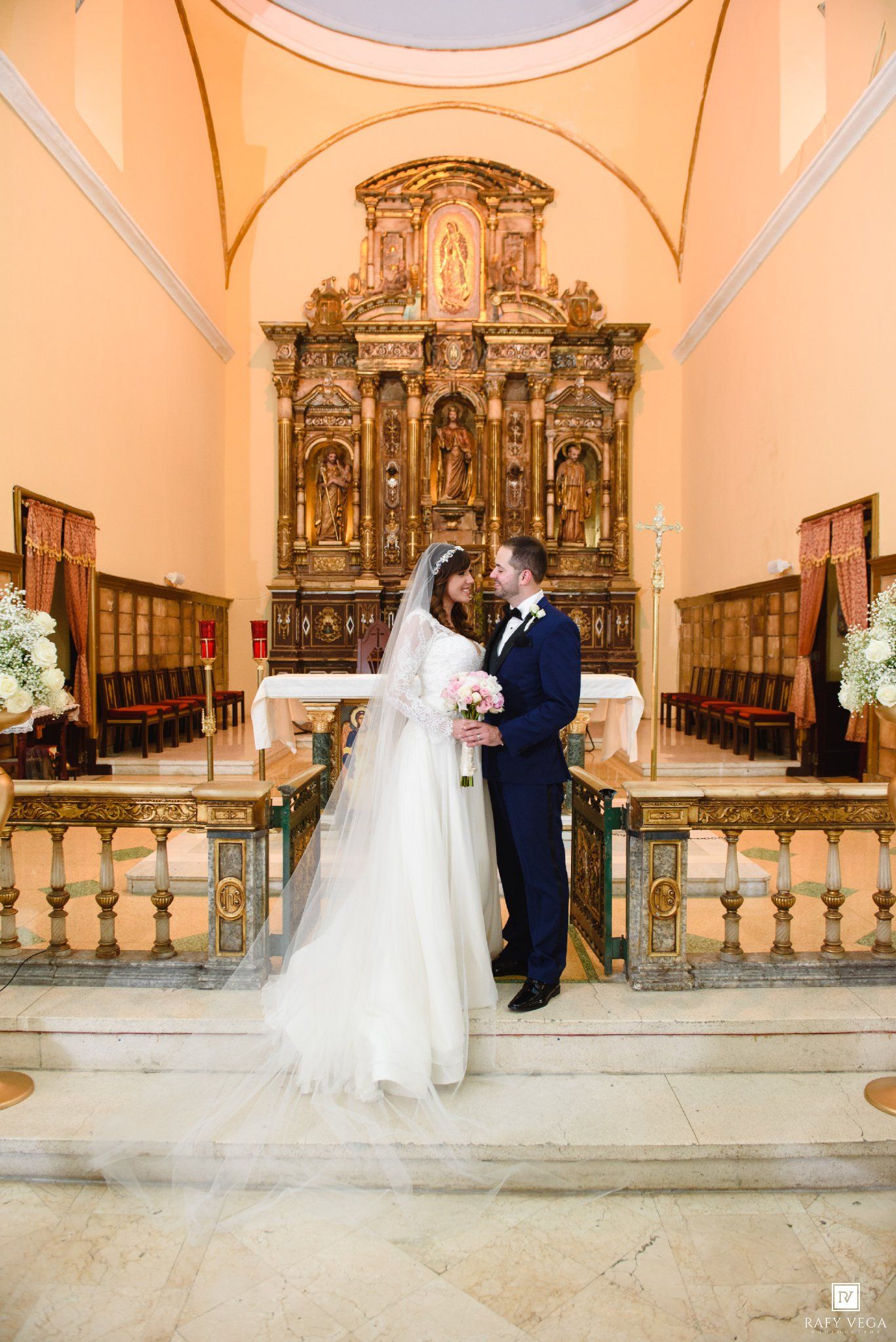 Bride and groom share a romantic moment at the ornate golden altar of a beautiful Catholic church.